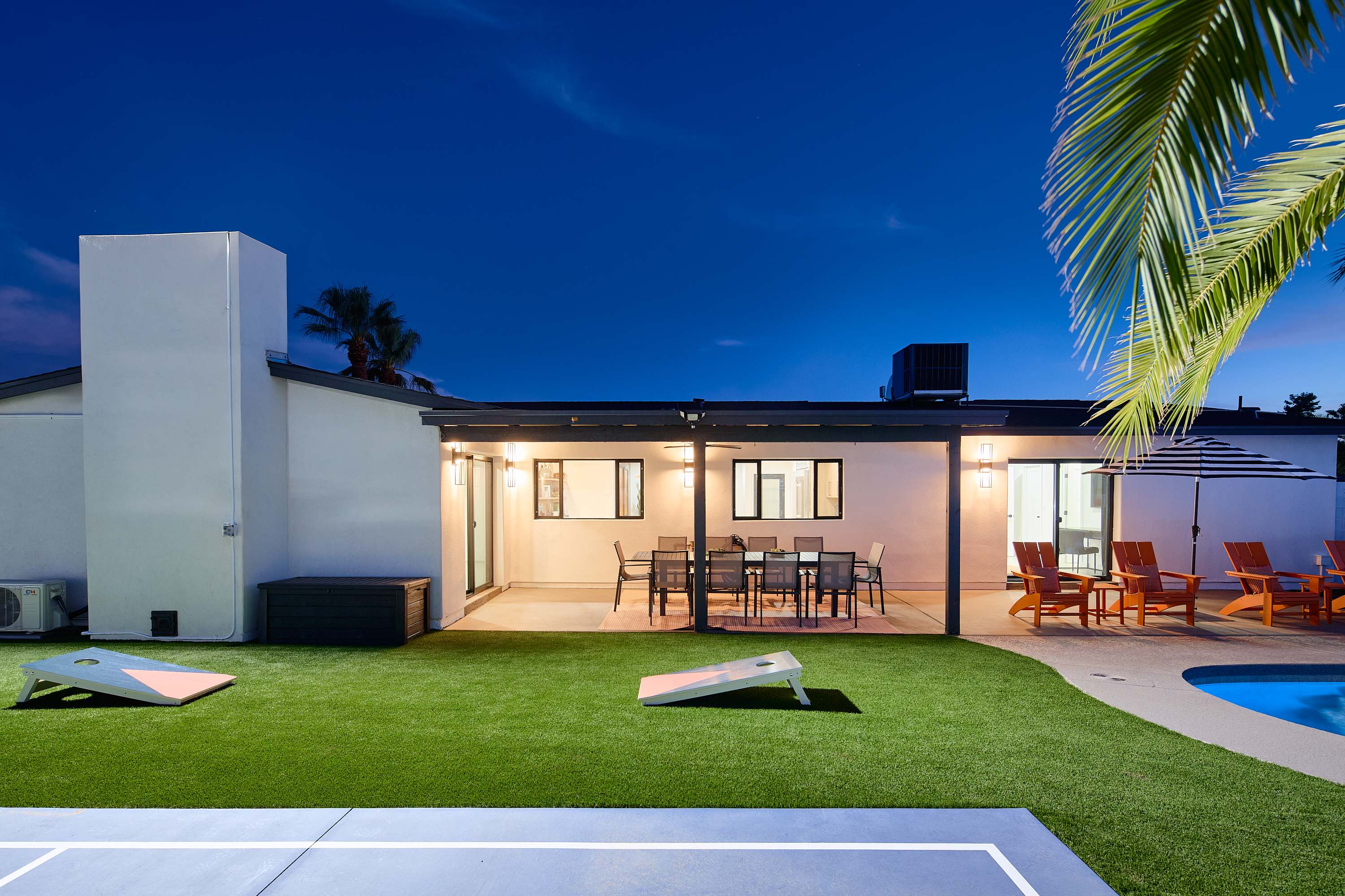 Resort-style backyard featuring a private pool, poolside loungers, a multi-sport court for basketball, pickleball, and tennis, turf with cornhole, a pergola with a built-in BBQ and bar seating, and a covered patio with outdoor dining table for 10.