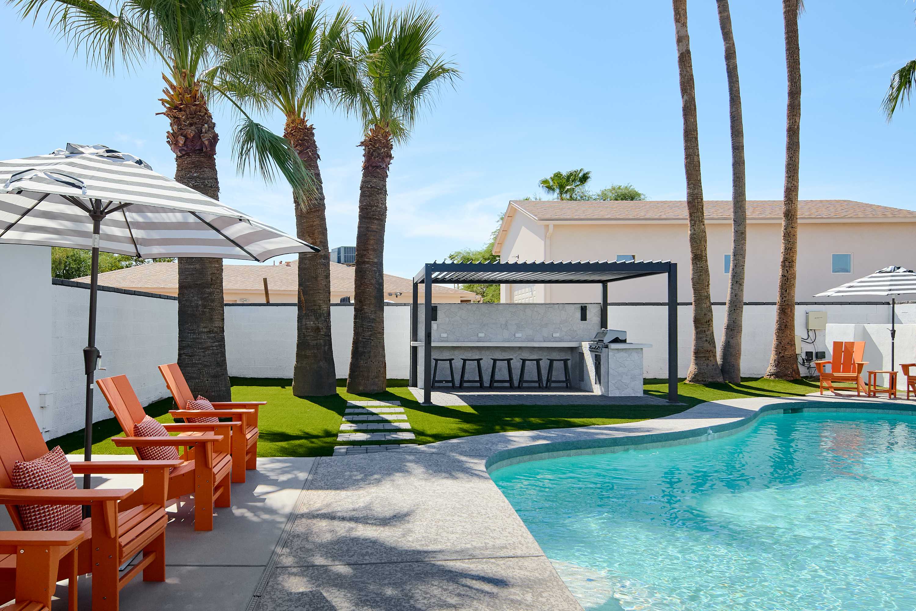 Private pool surrounded by poolside loungers, umbrellas, multiple shaded seating areas, and pergola with built in BBQ and bar seating.