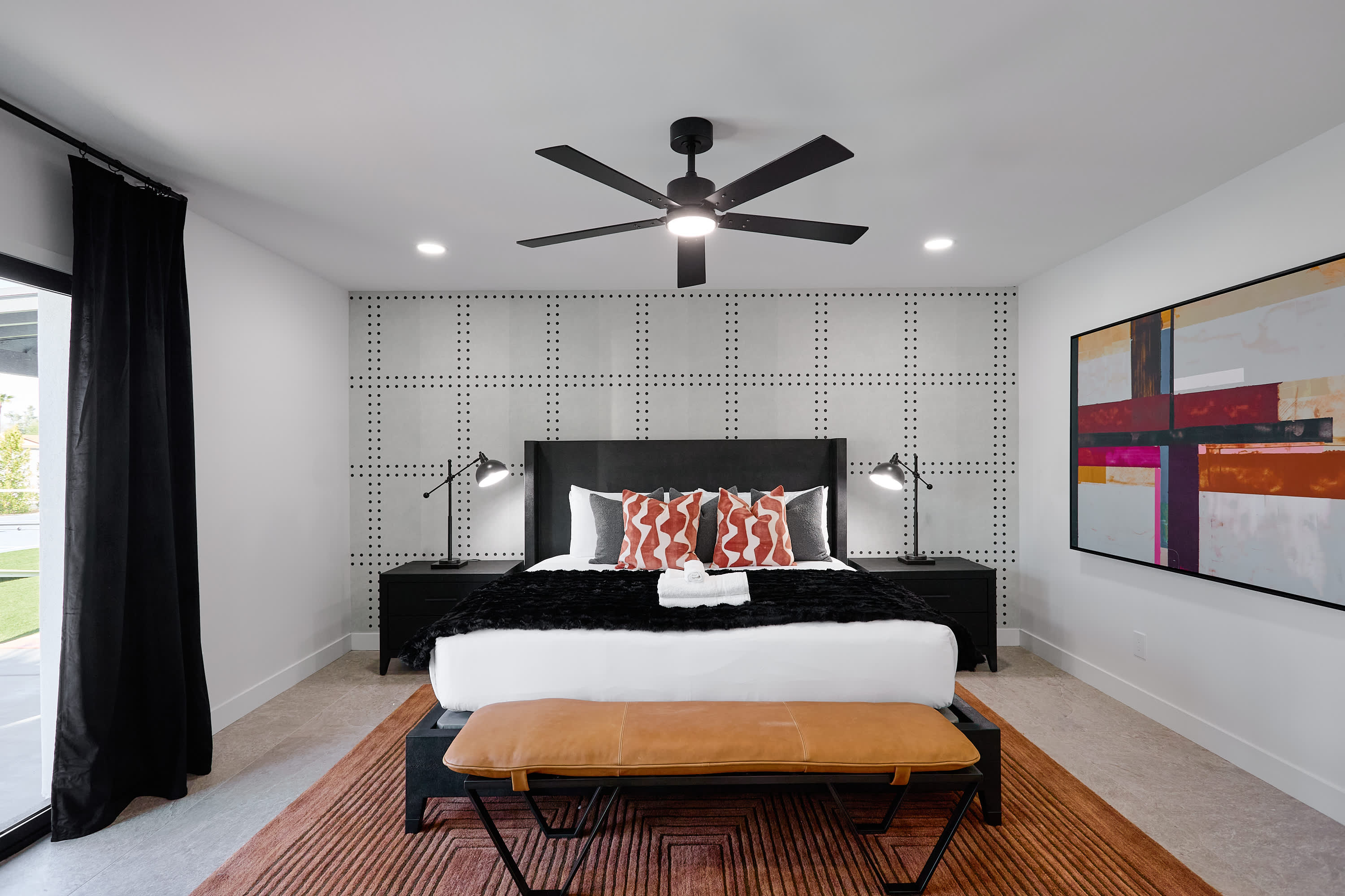 Primary bedroom with King bed, designer furnishings, walk-in closet, smart TV, ceiling fan, direct access to backyard, work station, and en-suite bathroom.