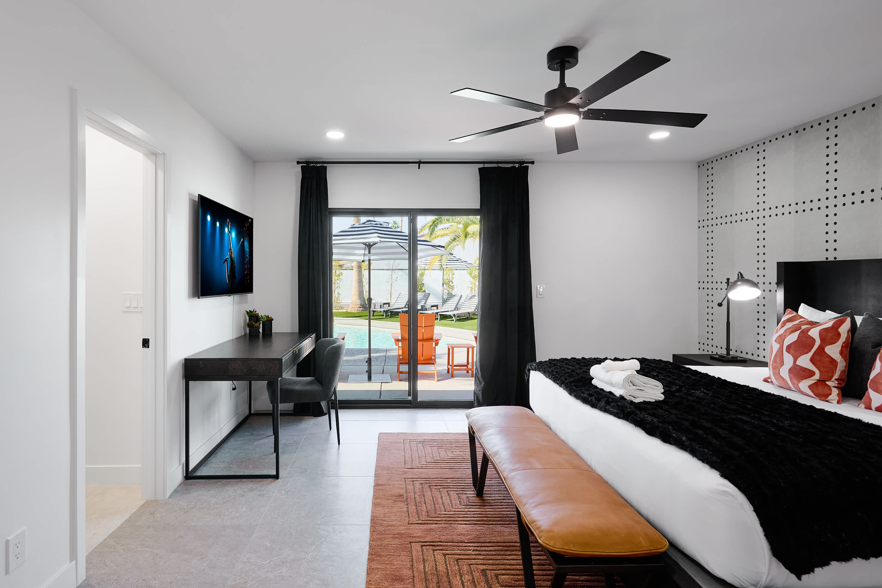 Primary bedroom with King bed, designer furnishings, walk-in closet, smart TV, ceiling fan, direct access to backyard, work station, and en-suite bathroom.