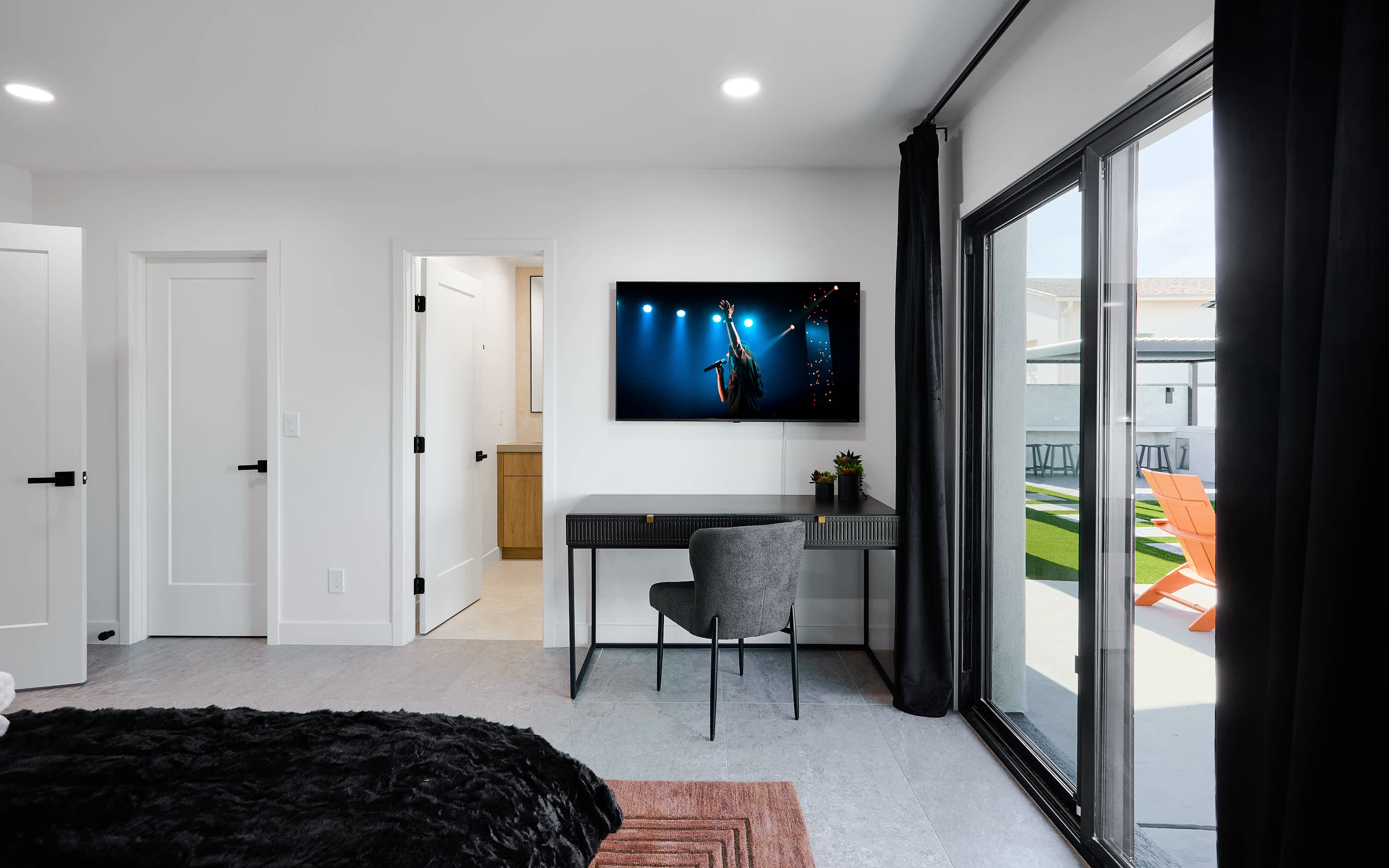Primary bedroom with King bed, designer furnishings, walk-in closet, smart TV, ceiling fan, direct access to backyard, work station, and en-suite bathroom.