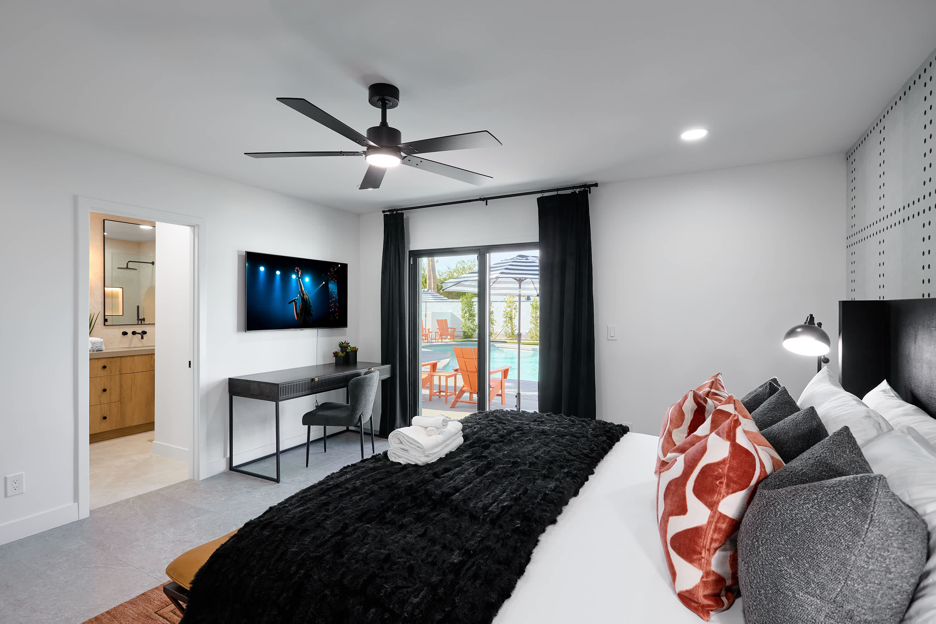 Primary bedroom with King bed, designer furnishings, walk-in closet, smart TV, ceiling fan, direct access to backyard, work station, and en-suite bathroom.