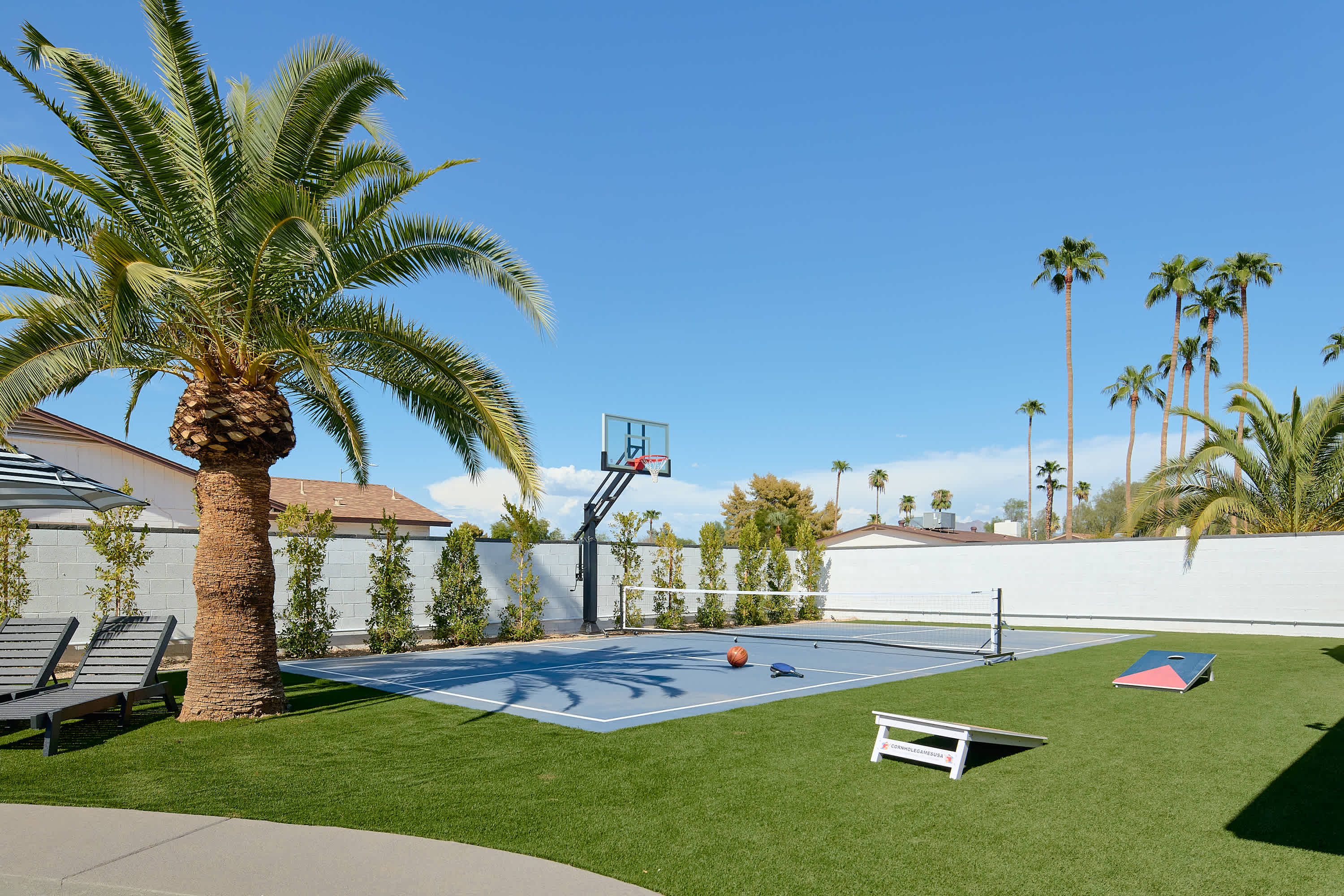 Resort-style backyard featuring a private pool, poolside loungers, a multi-sport court for basketball, pickleball, and tennis, turf with cornhole, a pergola with a built-in BBQ and bar seating, and a covered patio with outdoor dining table for 10.