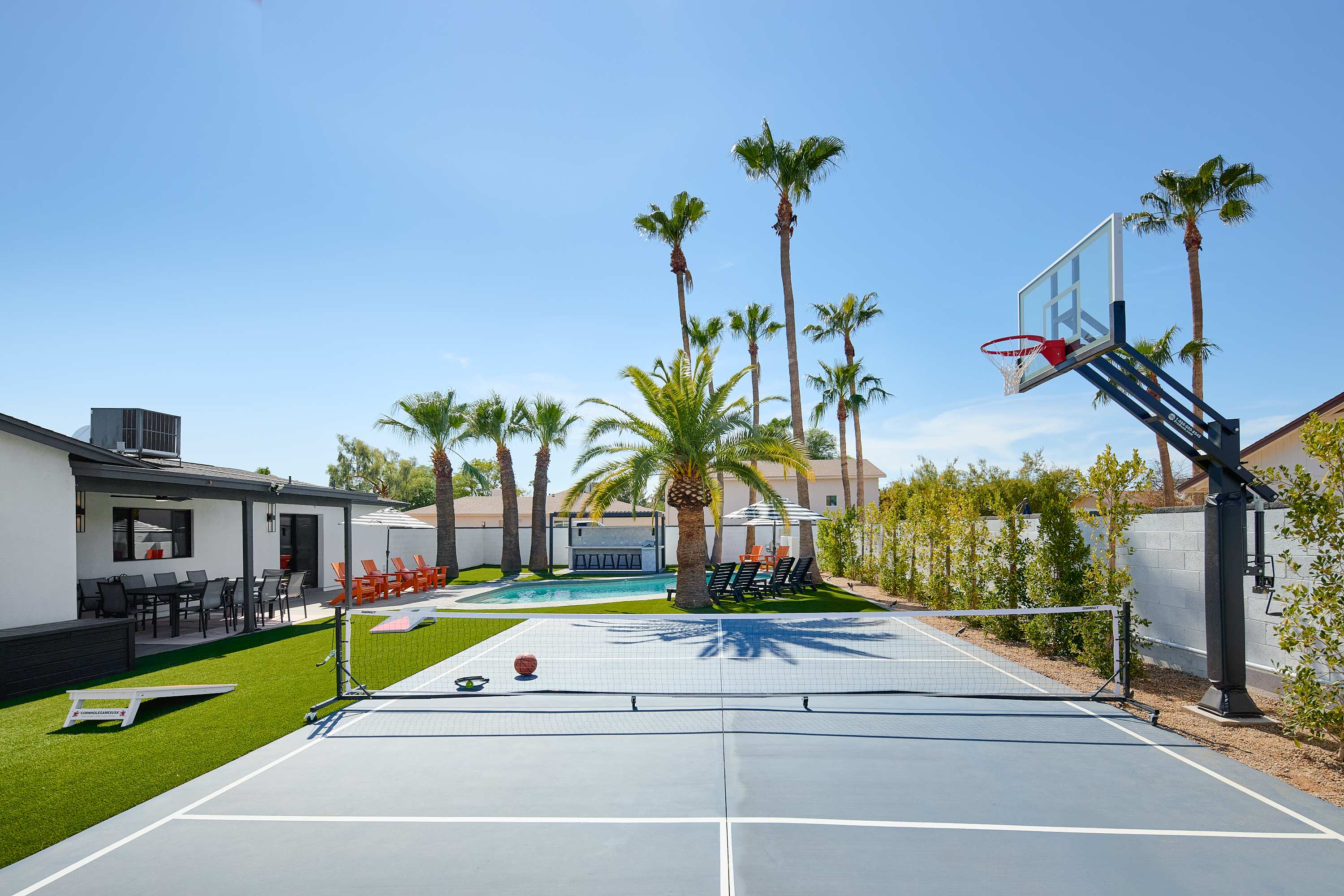 Resort-style backyard featuring a private pool, poolside loungers, a multi-sport court for basketball, pickleball, and tennis, turf with cornhole, a pergola with a built-in BBQ and bar seating, and a covered patio with outdoor dining table for 10.
