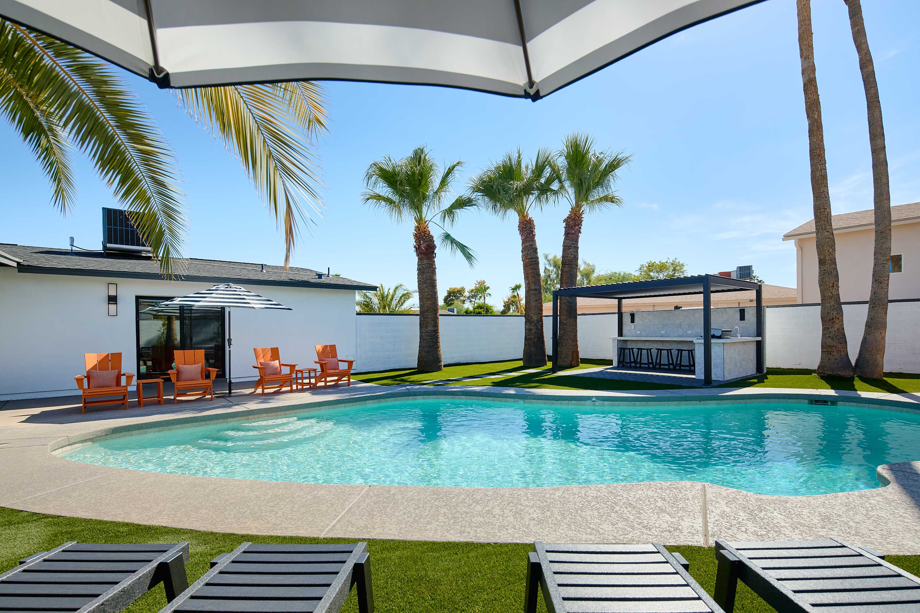 Private pool surrounded by poolside loungers, umbrellas, multiple shaded seating areas, and pergola with built in BBQ and bar seating.