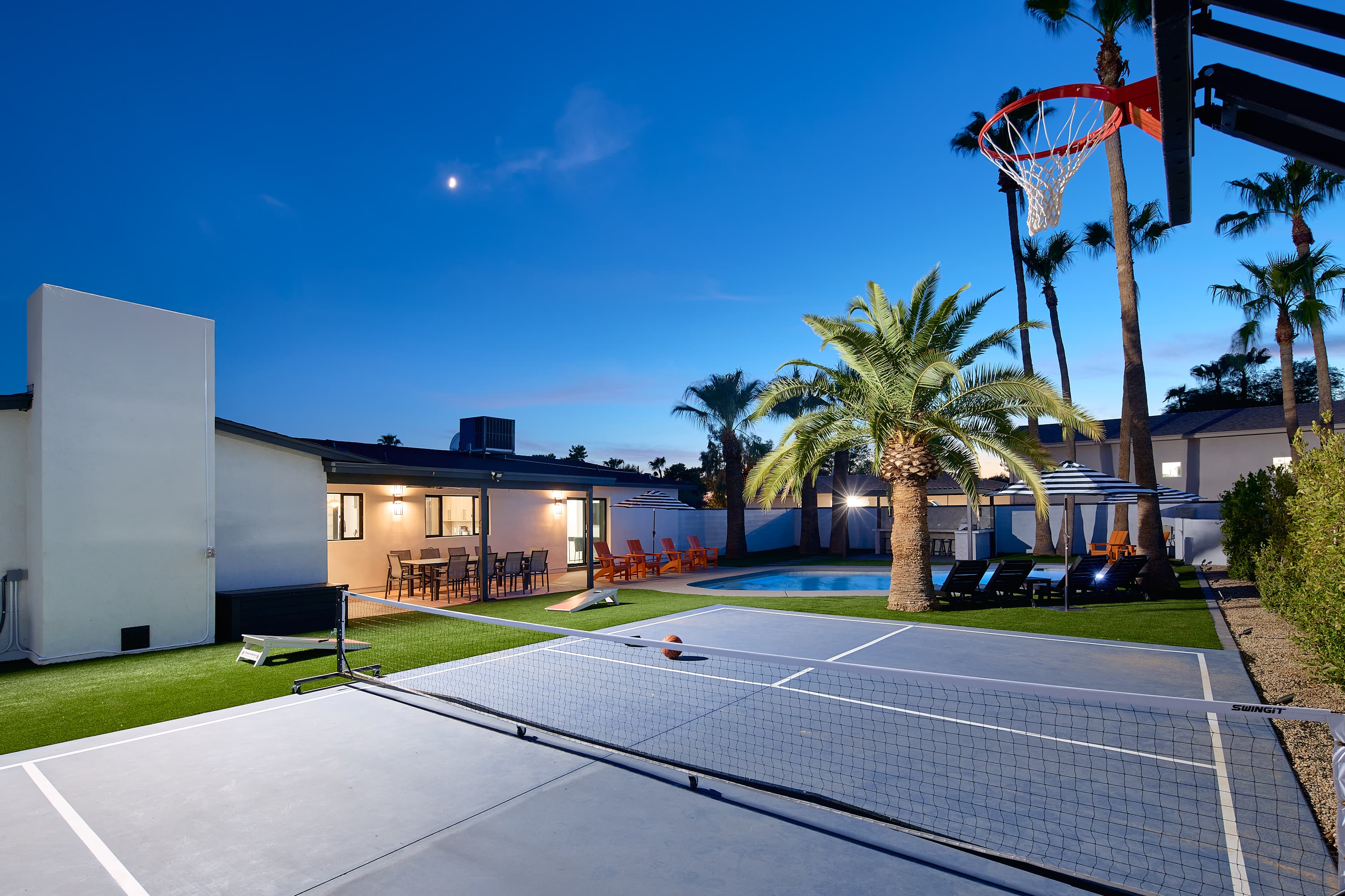 Resort-style backyard featuring a private pool, poolside loungers, a multi-sport court for basketball, pickleball, and tennis, turf with cornhole, a pergola with a built-in BBQ and bar seating, and a covered patio with outdoor dining table for 10.