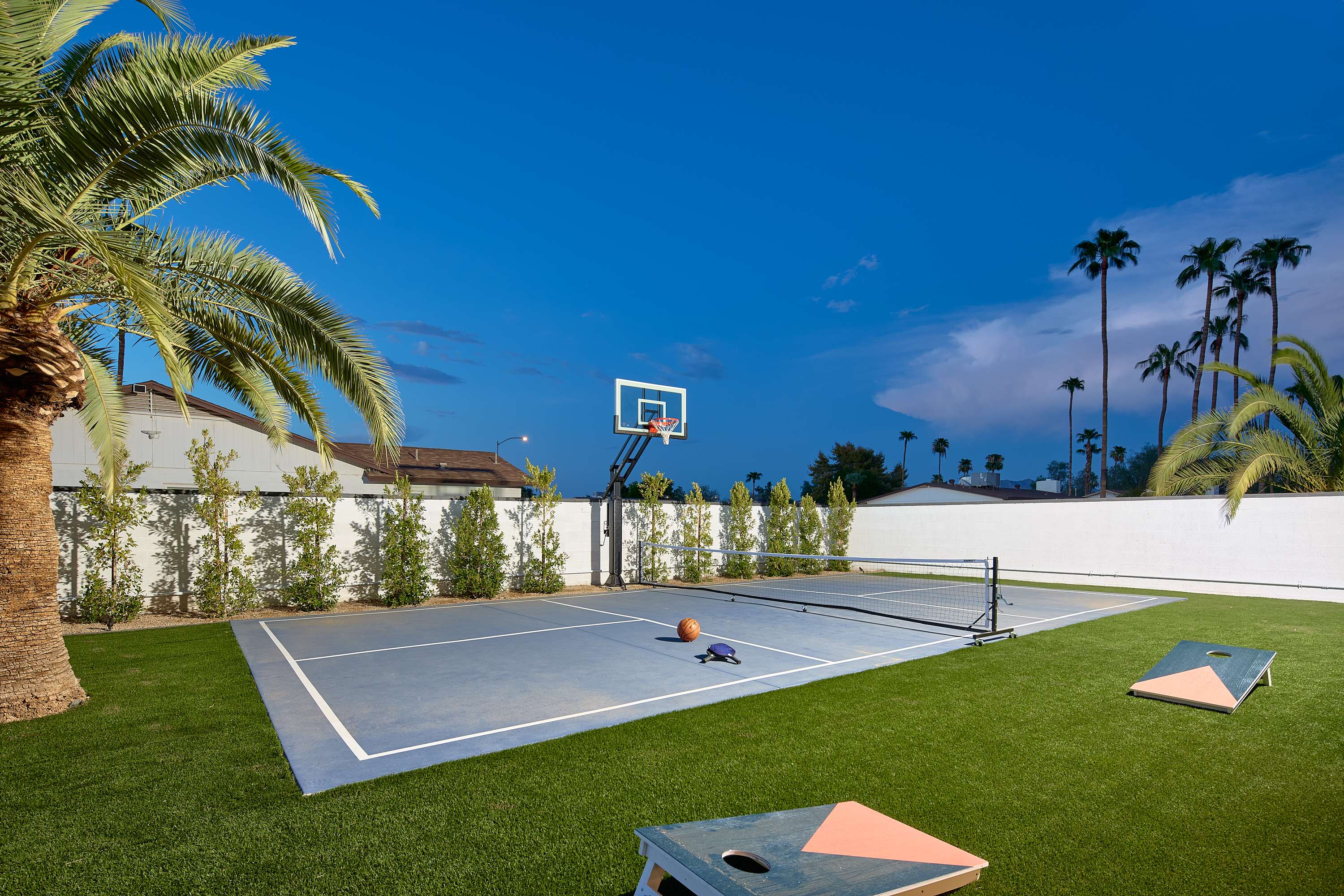 Private multi-sport court for basketball, pickleball, and tennis beside a spacious turf lawn with cornhole for even more outdoor fun.