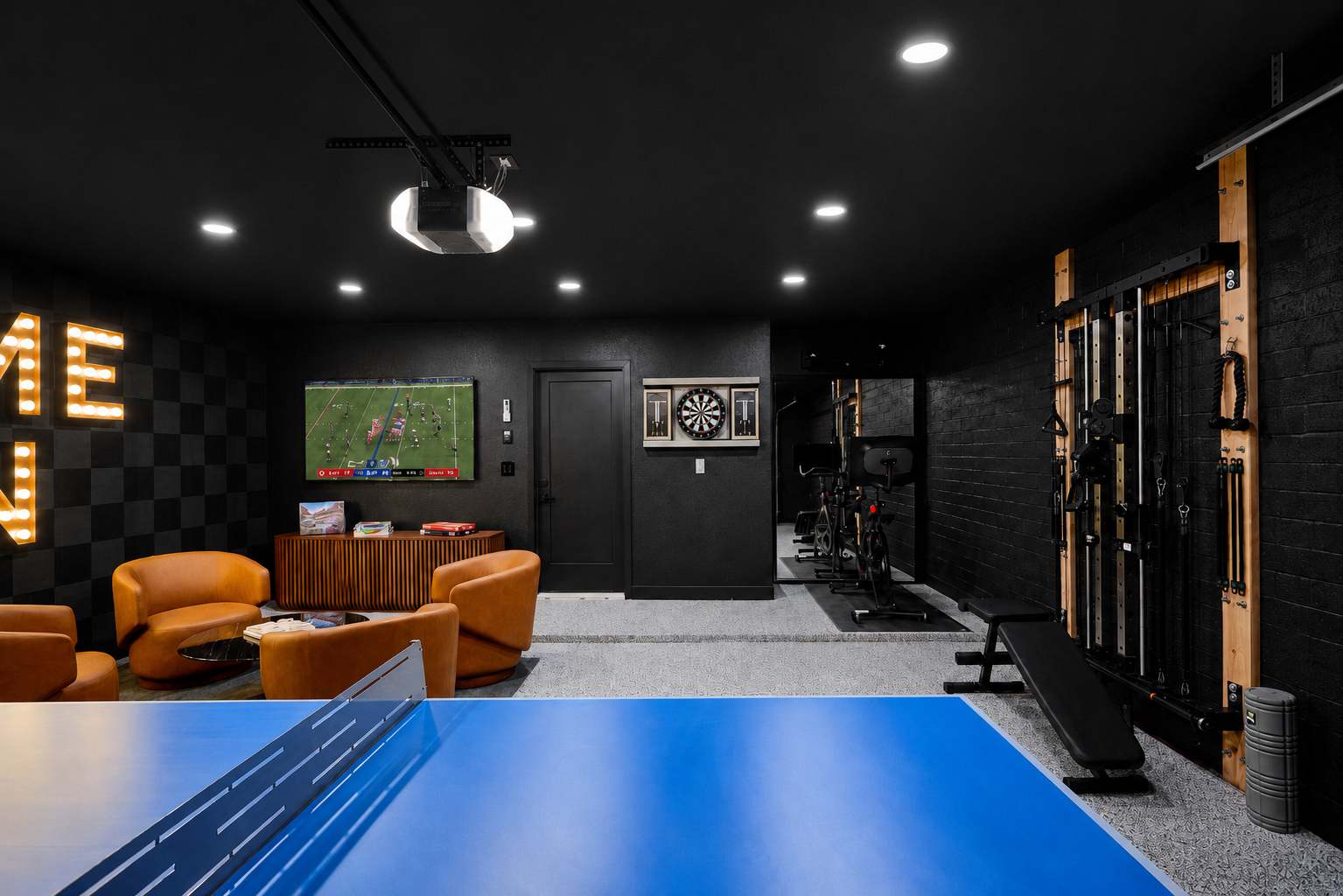 Game room and home gym packed with indoor entertainment, featuring a Peloton bike, ping pong table, arcade game, darts, TV, lounge seating, and a wall-mounted gym system.