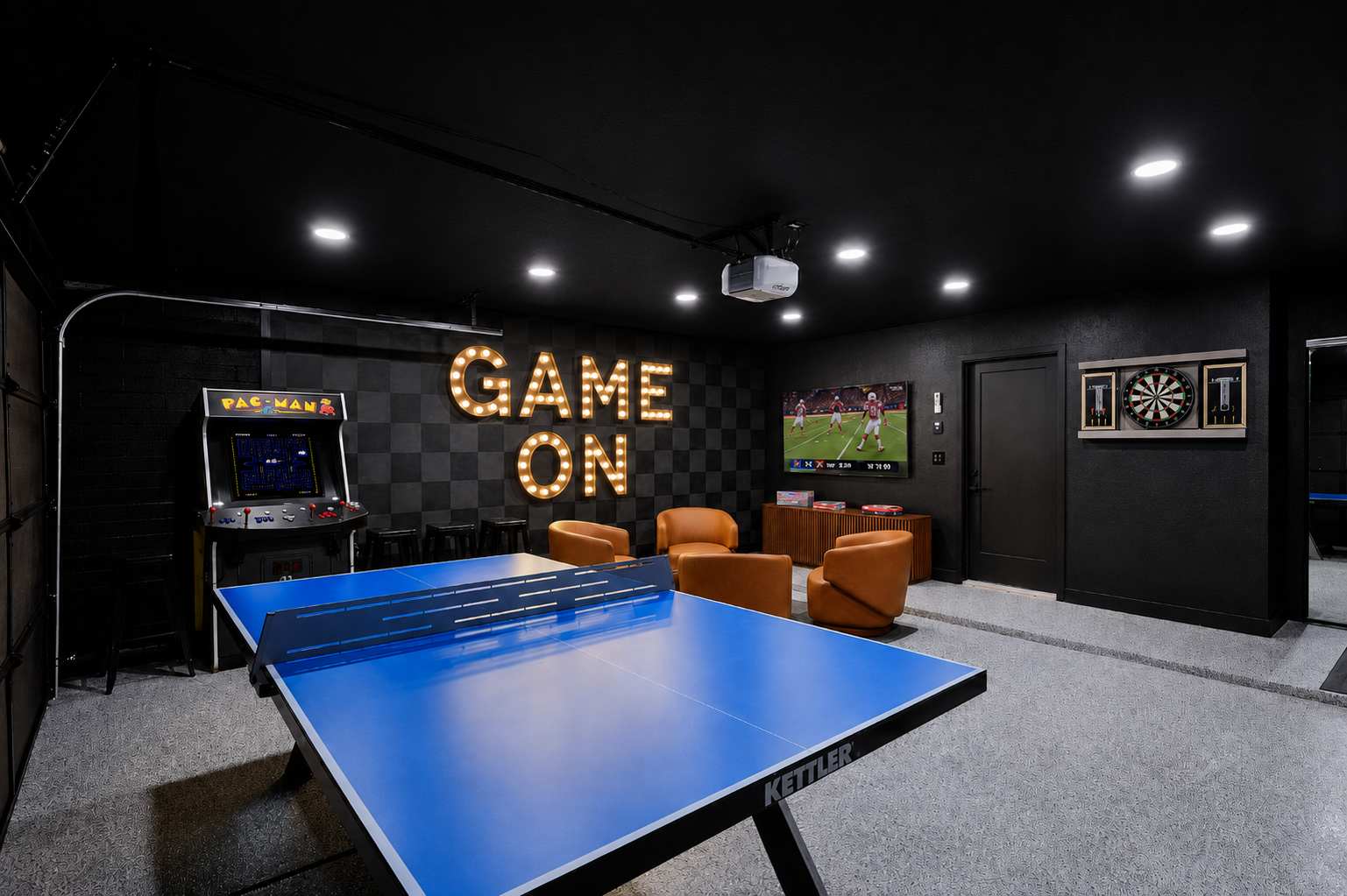Game room and home gym packed with indoor entertainment, featuring a Peloton bike, ping pong table, arcade game, darts, TV, lounge seating, and a wall-mounted gym system.