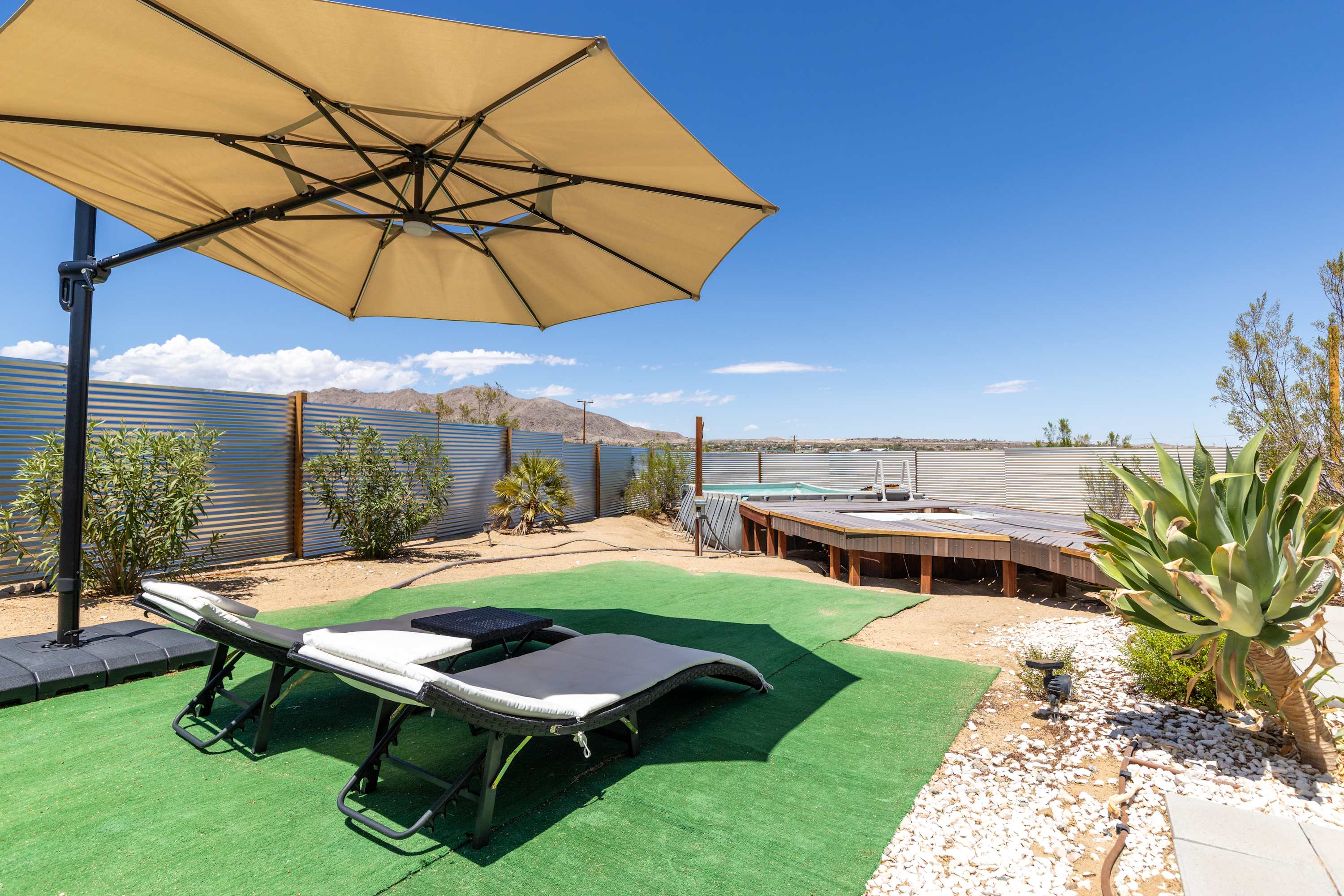 Two outdoor loungers on the studio courtyard turf beneath a shade umbrella.
