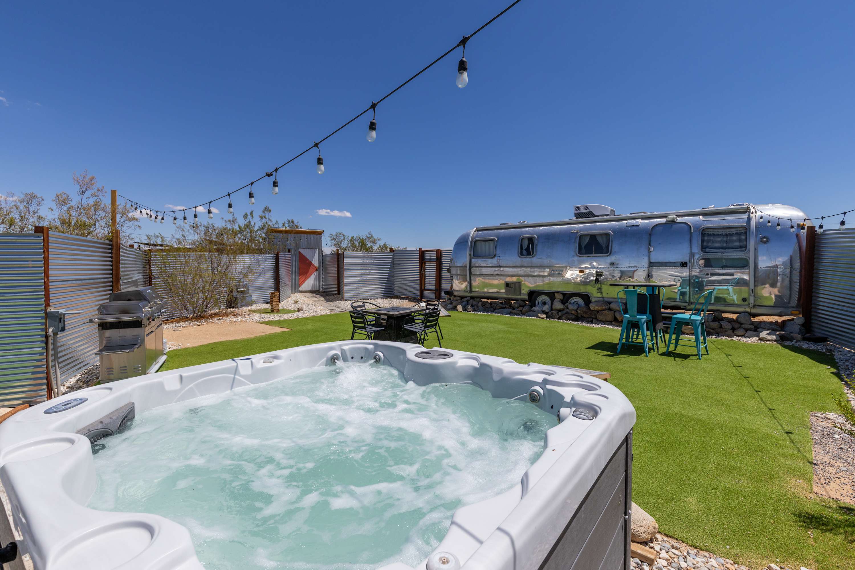 Airstream courtyard spa with bubbling water, string lights and the trailer behind it.