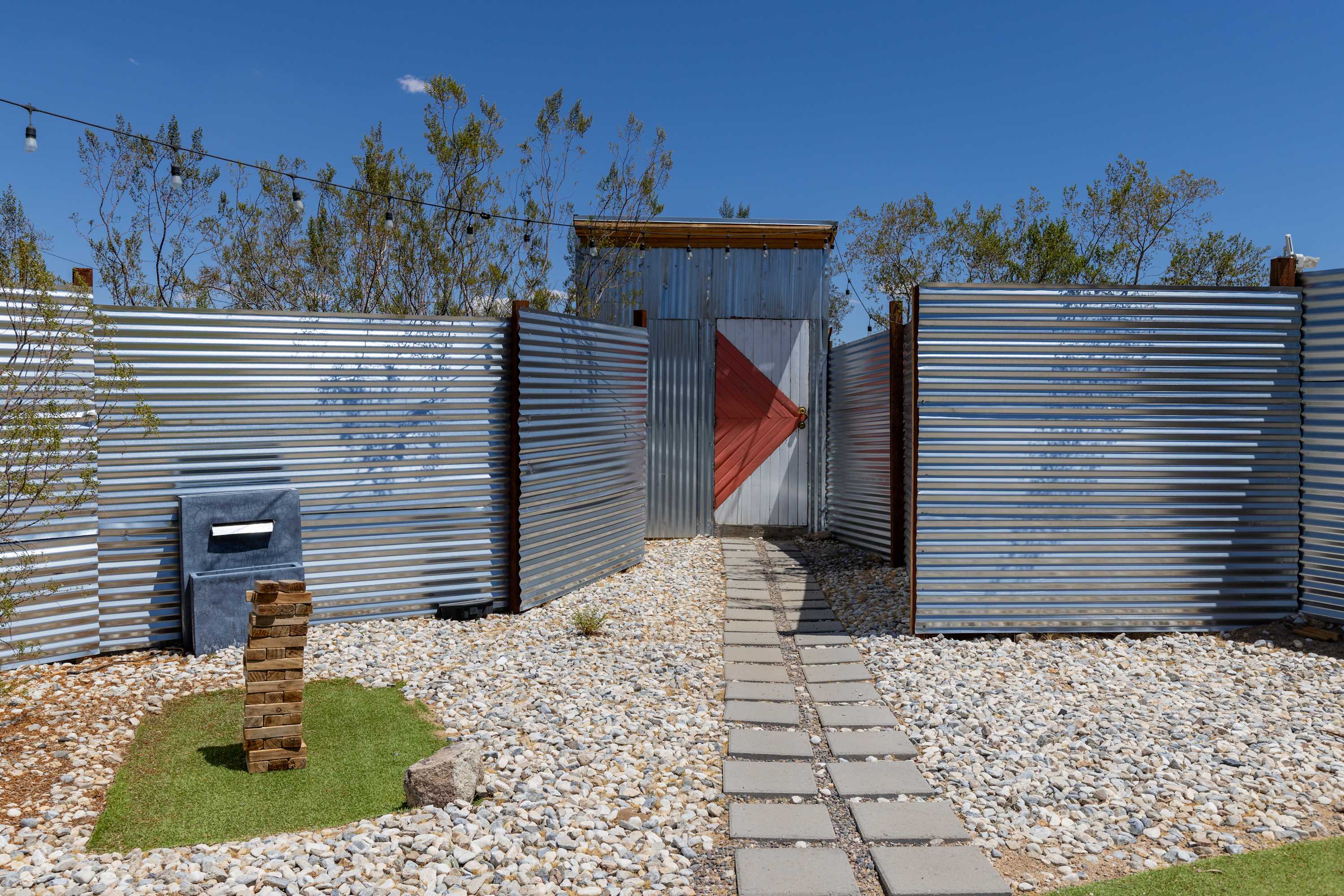 Daytime entrance gate to the Airstream courtyard, with corrugated metal fencing and a stone path.