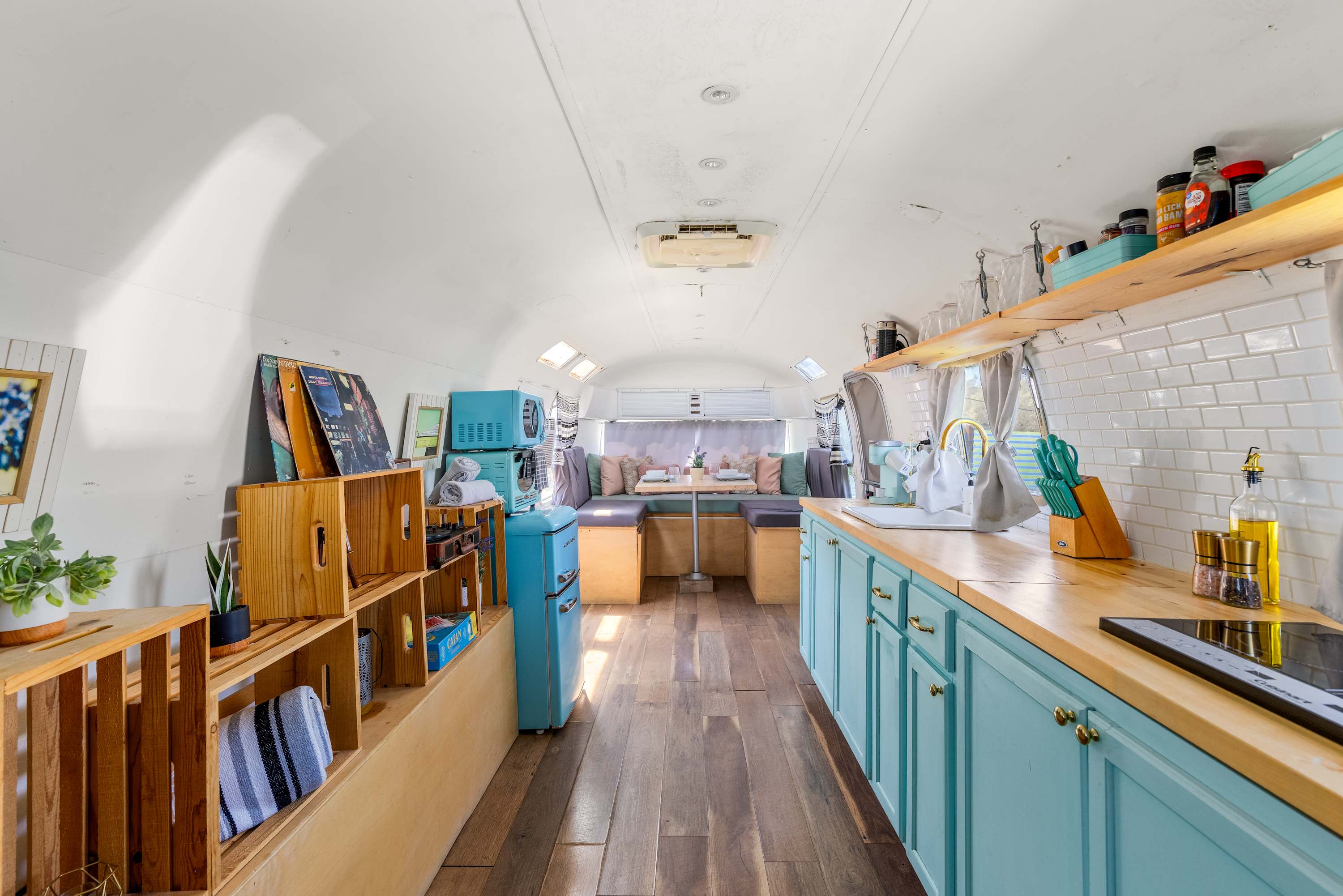 Wide Airstream interior with pale-blue kitchenette cabinets, wood counters and dining seating.