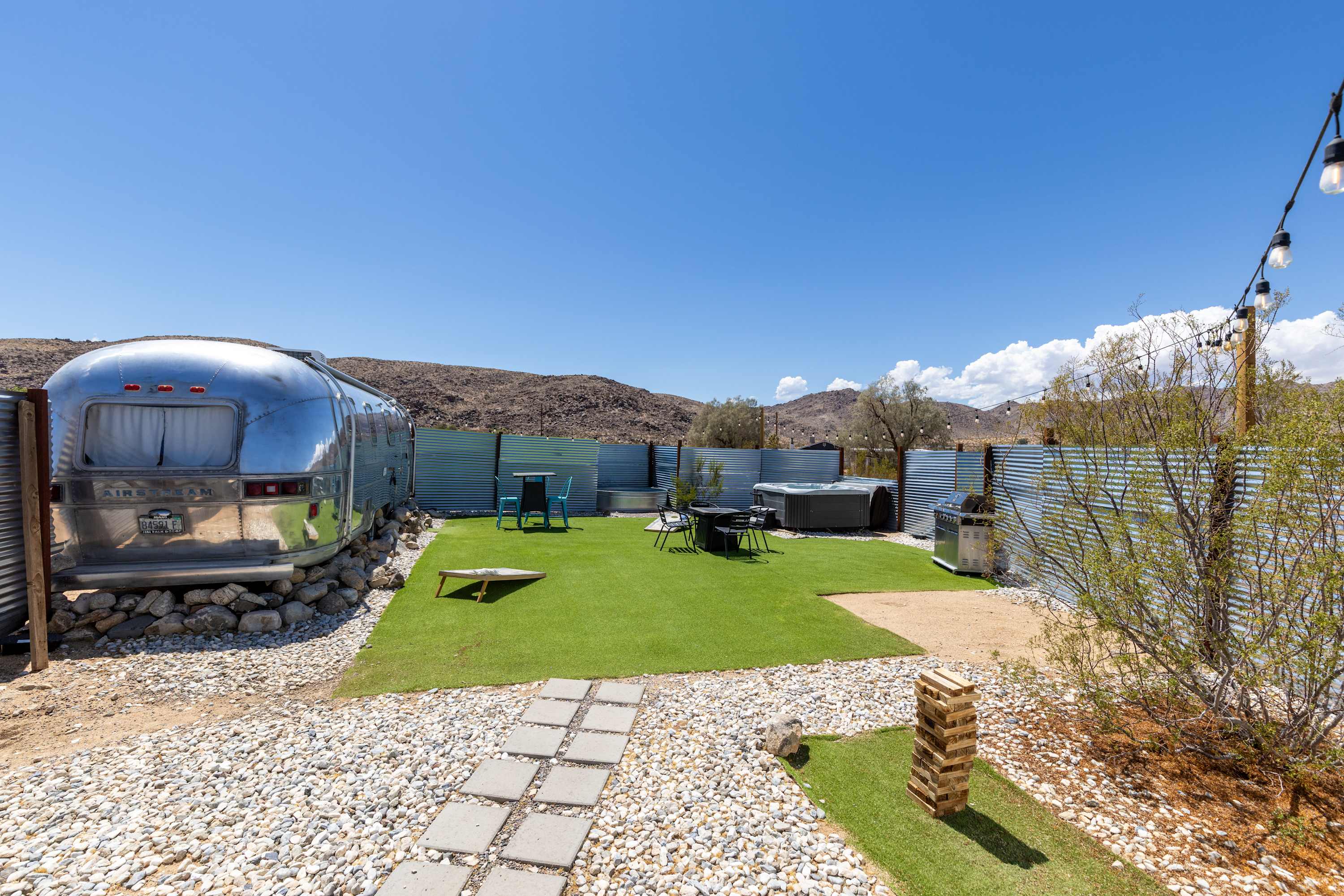 Wide Airstream courtyard view with turf, a stone path, dining table and lawn games.
