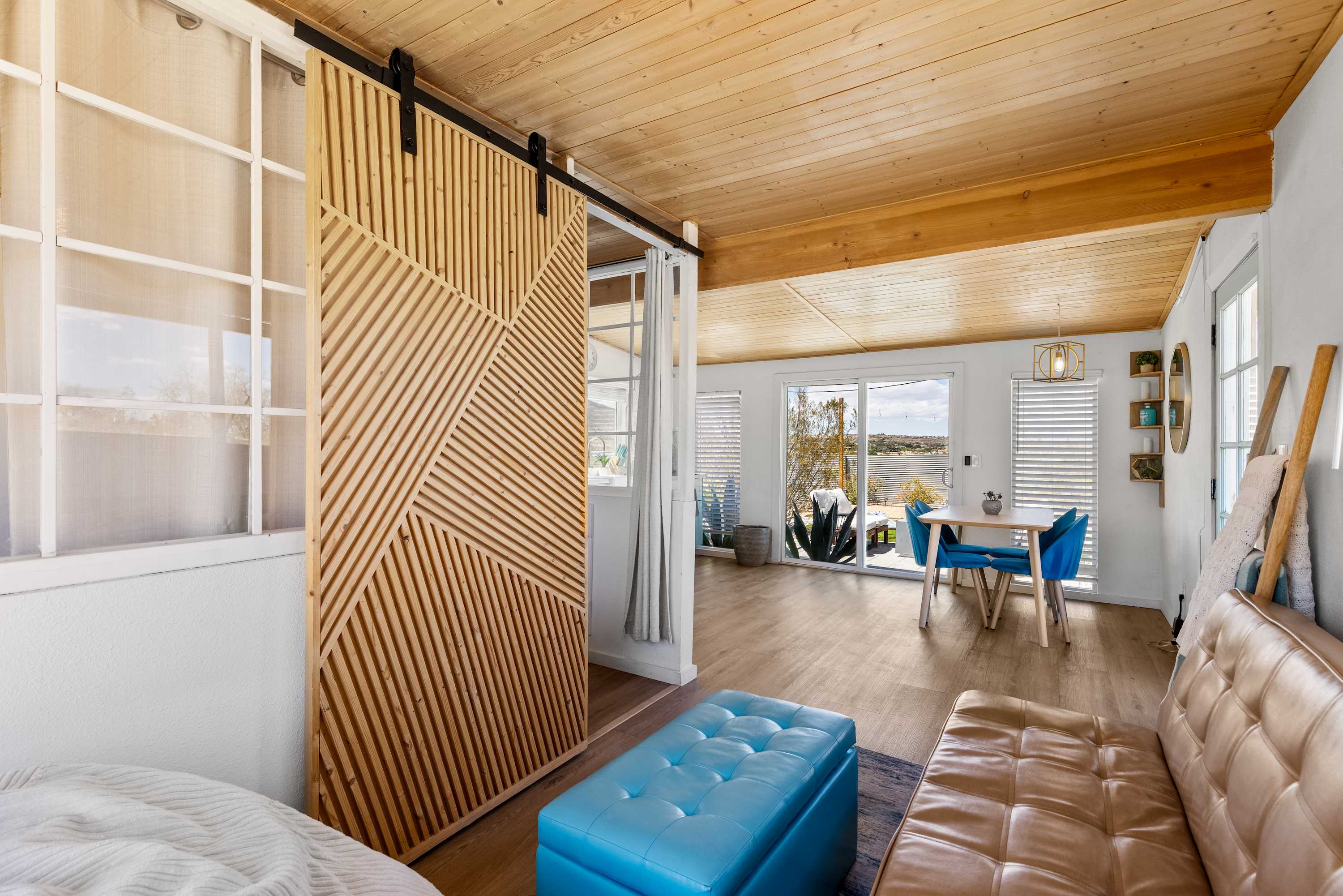 Studio seating area with a brown sofa, blue ottoman and slatted bedroom divider.
