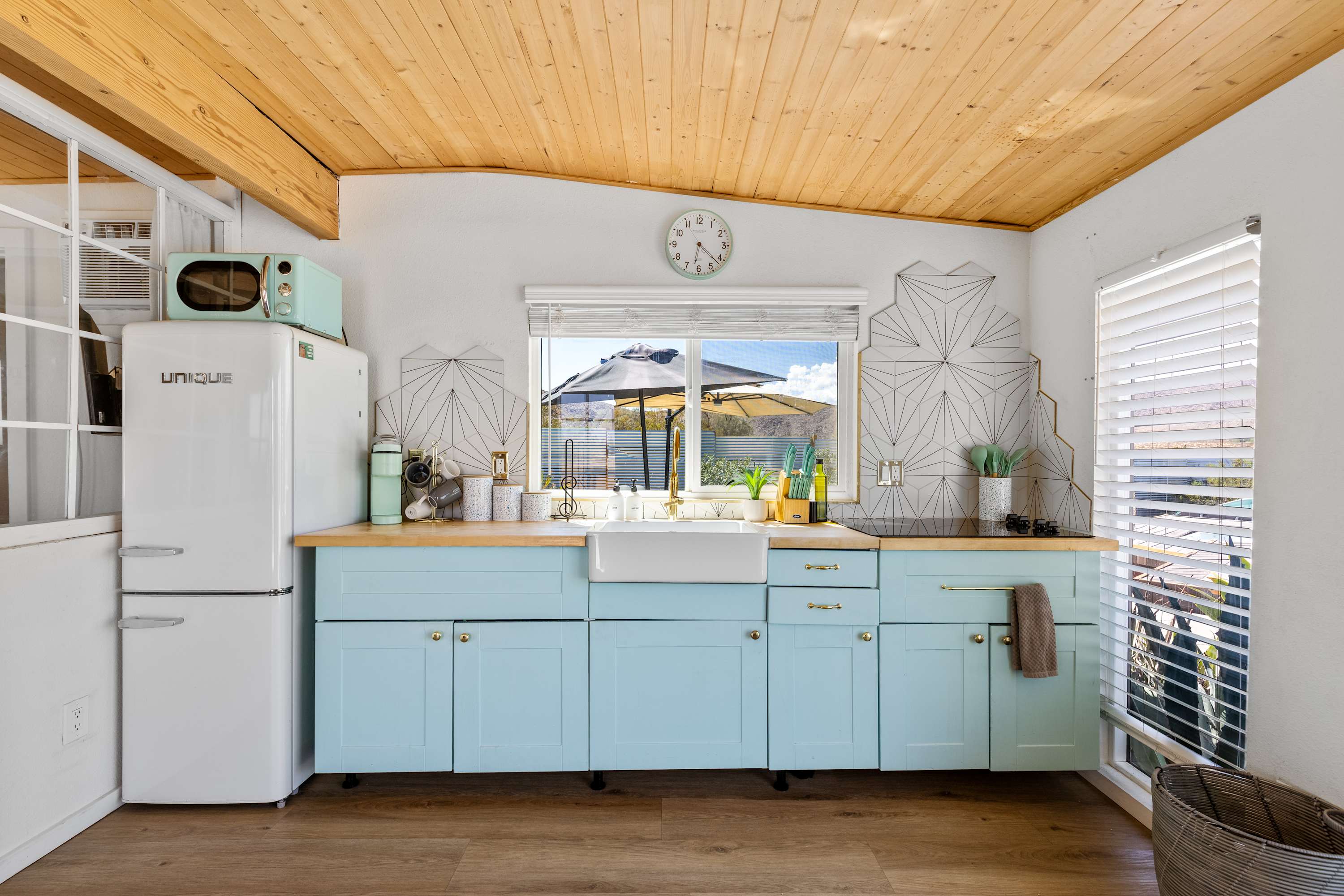 Studio kitchen with pale-blue cabinets, white counters, a farmhouse sink and refrigerator.