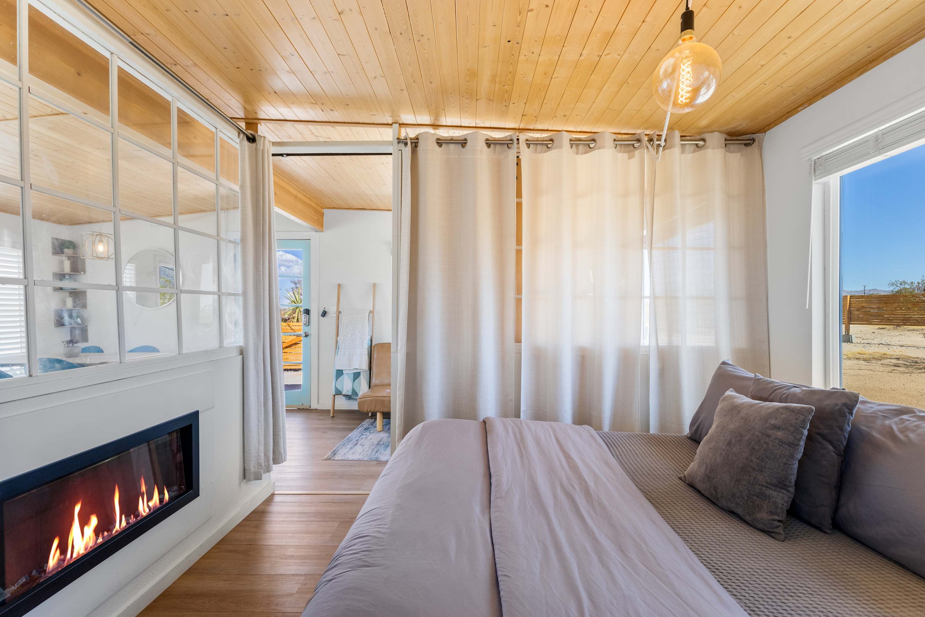 Studio sleeping area with curtains, windows, a gray bed and a wall-mounted fireplace.