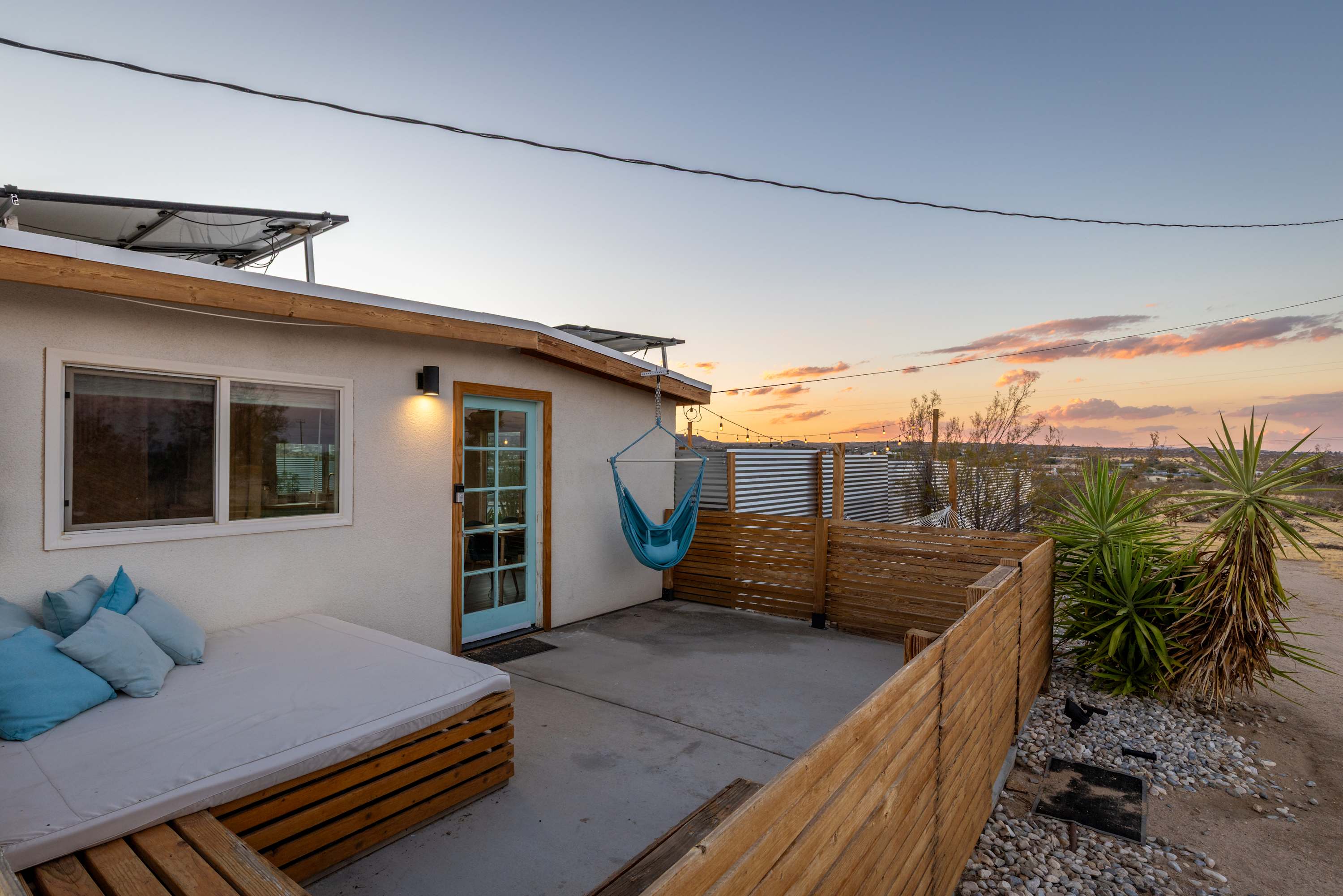Studio rear patio at sunset with cushioned outdoor seating, wood decking and a hammock chair.