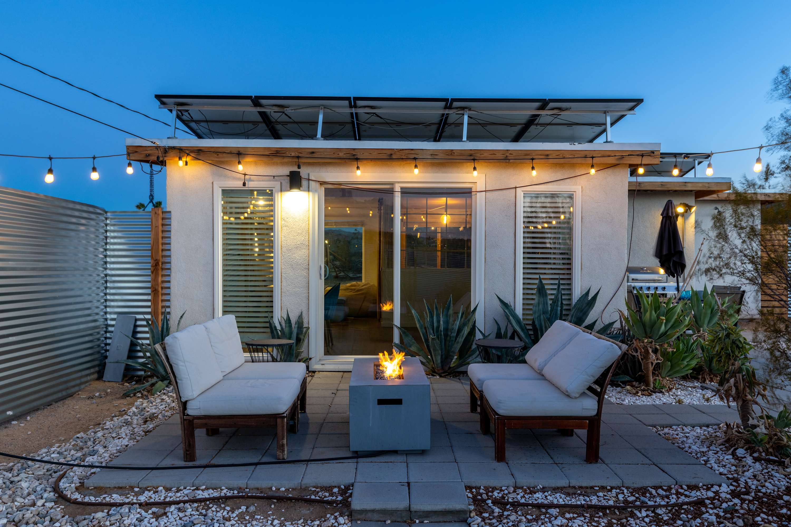 Studio front patio at dusk with two cushioned chairs and a lit fire table.