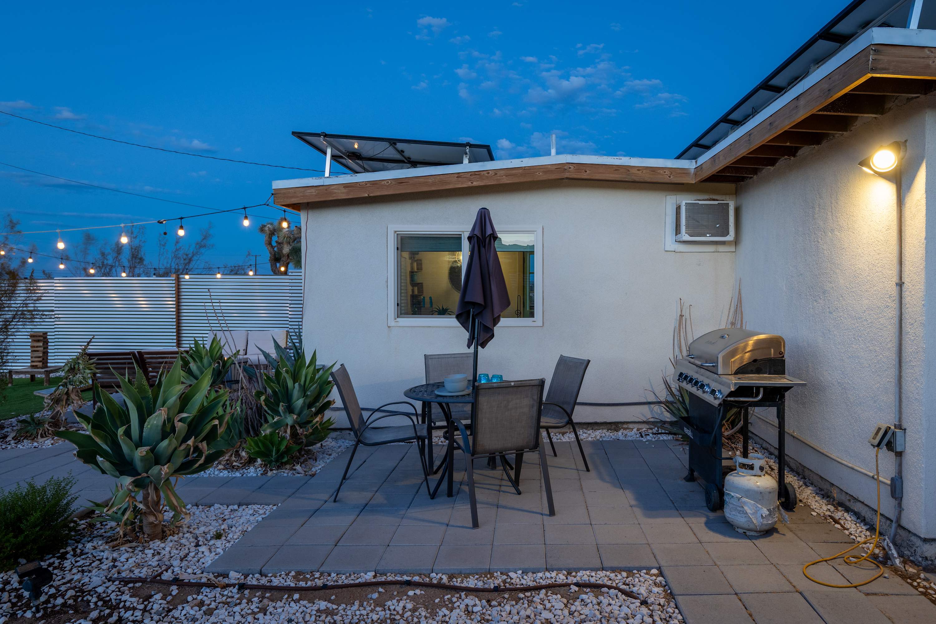 Studio side courtyard at dusk with an outdoor dining table, umbrella and grill.