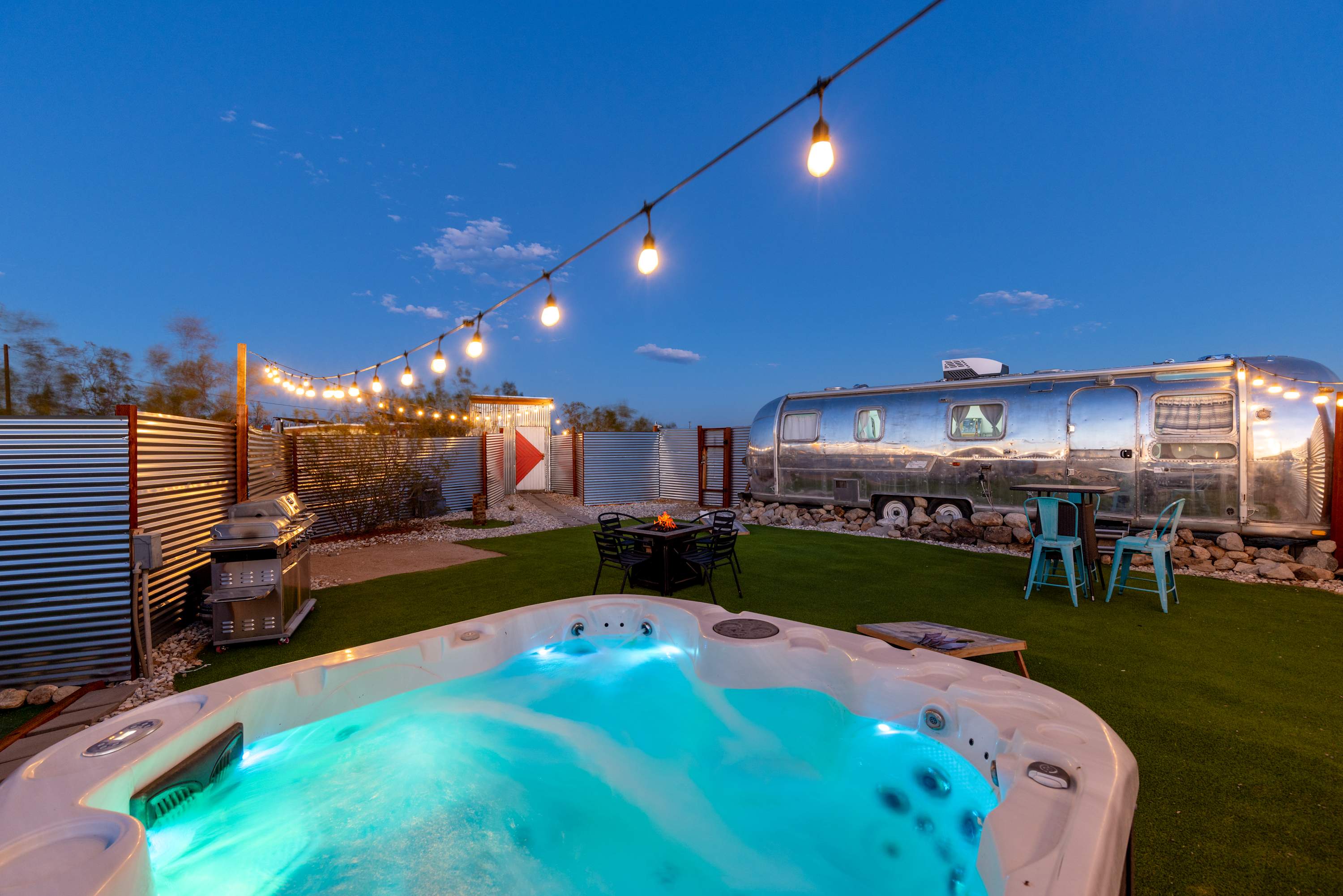 Illuminated Airstream courtyard spa beneath string lights at dusk.