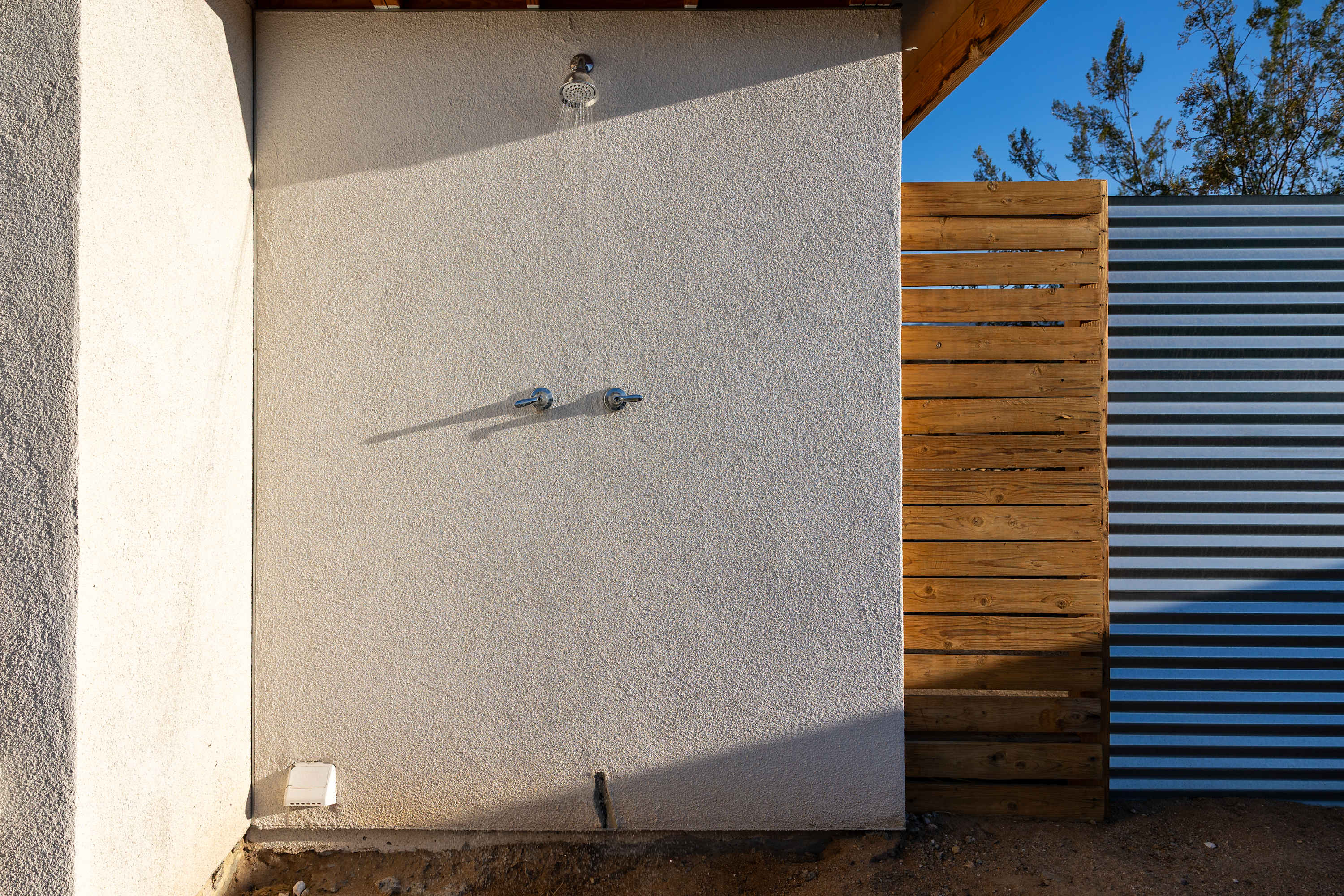 Wall-mounted outdoor water fixture beside the studio courtyard and wood gate.