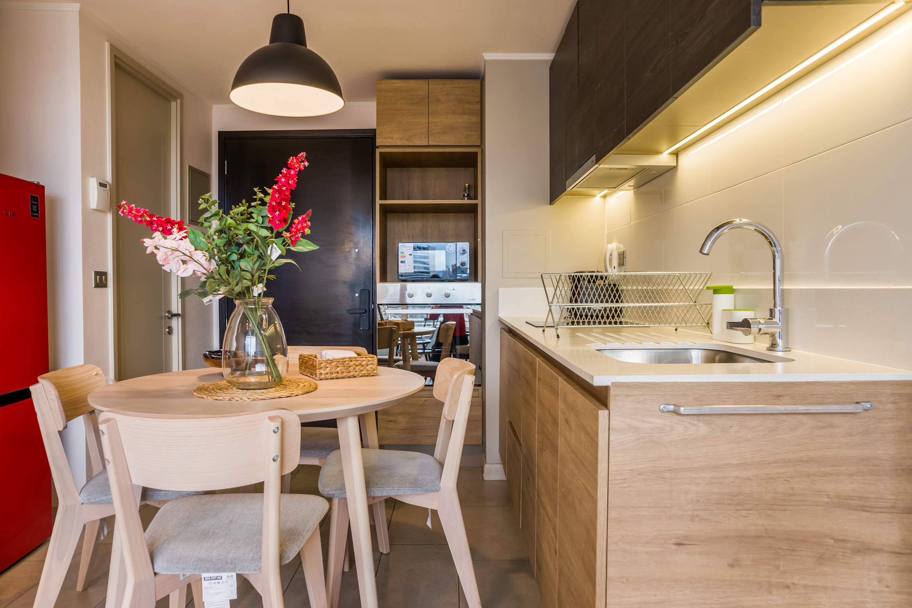 Private kitchen with wood cabinetry, a round dining table, and a bright red refrigerator, designed for convenient meals in a compact apartment.