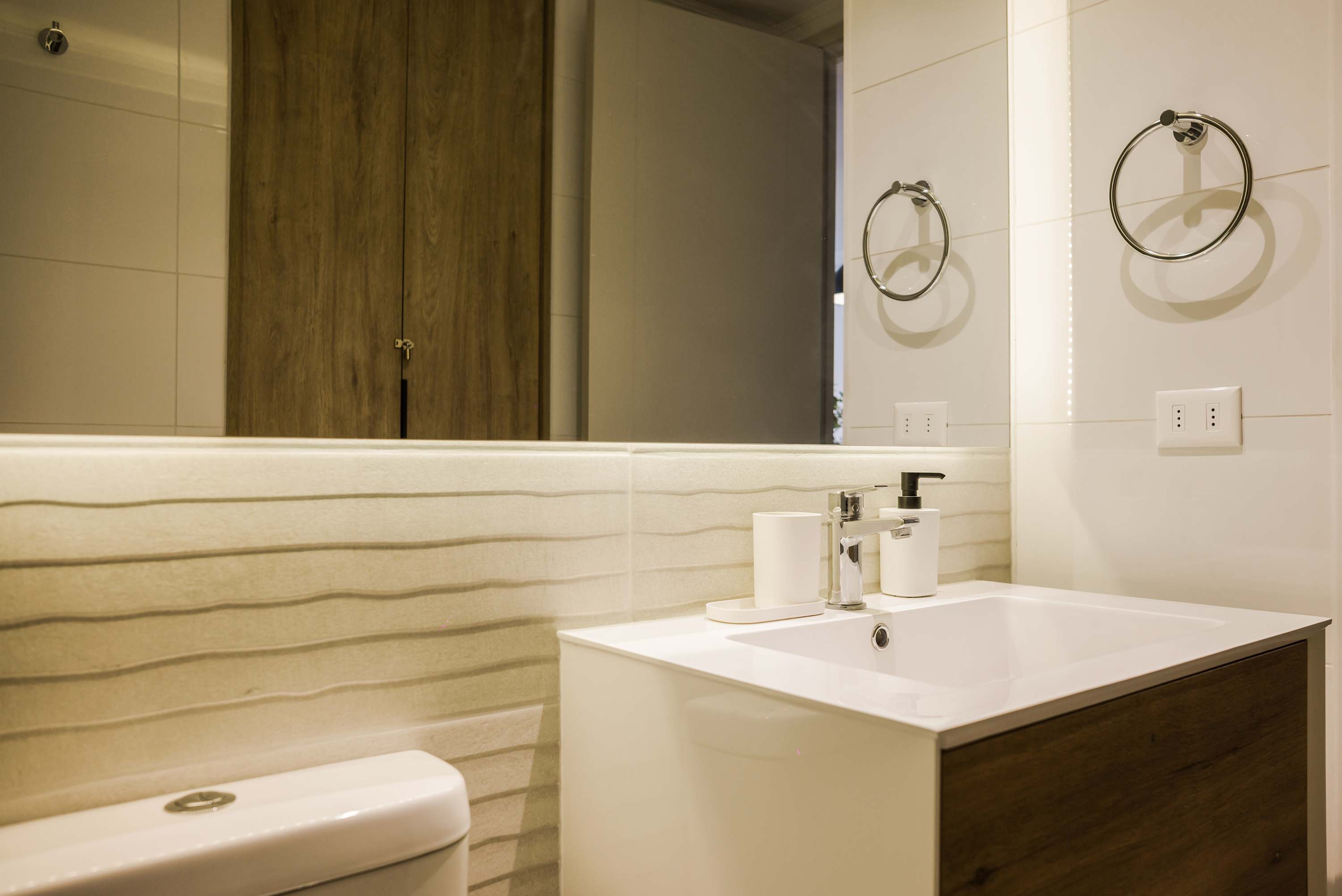 Modern bathroom with a spacious mirrored vanity, chrome fixtures, and warm wood cabinetry.