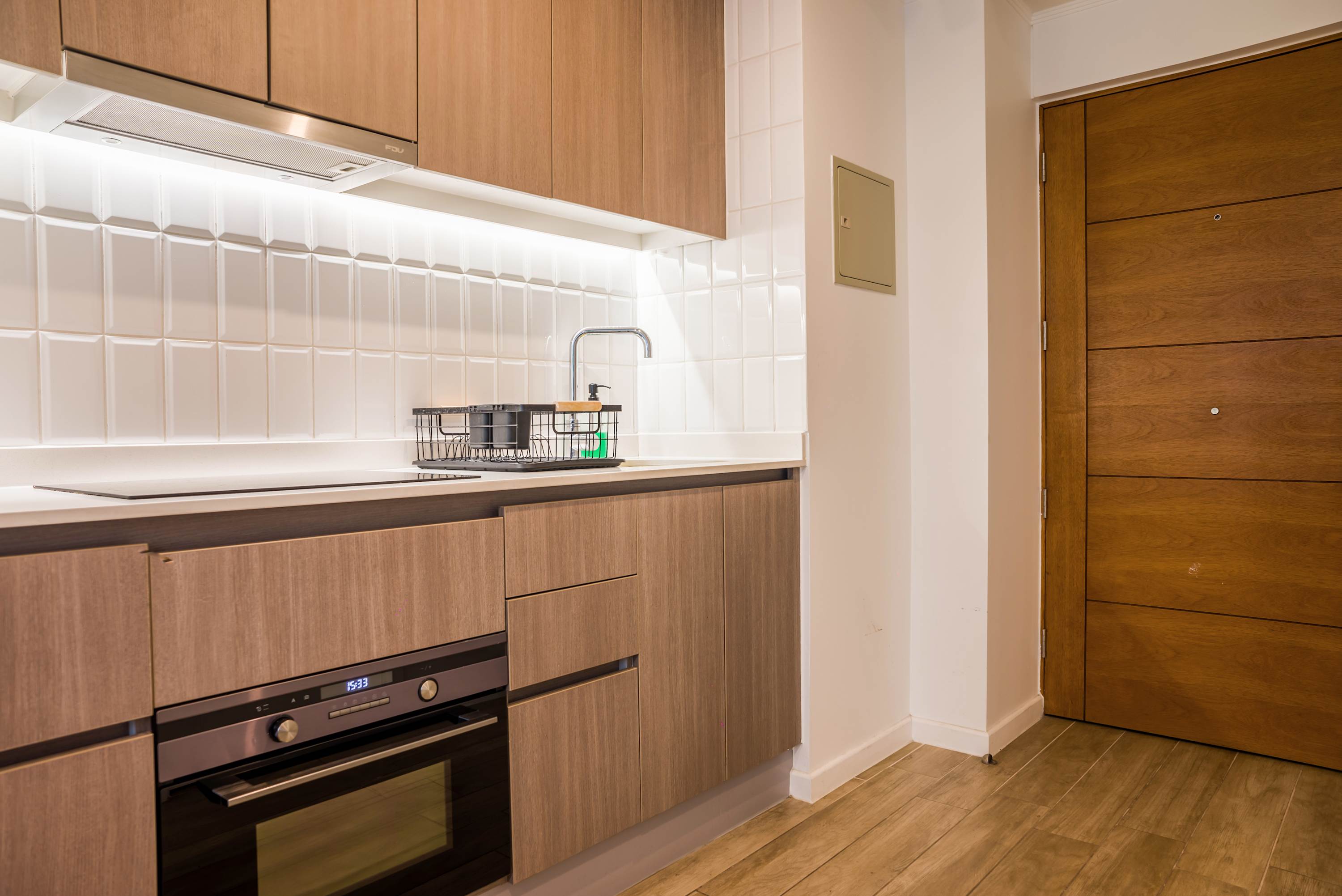 Private kitchen with wood cabinetry, induction cooktop, built-in oven, and a bright tiled backsplash.