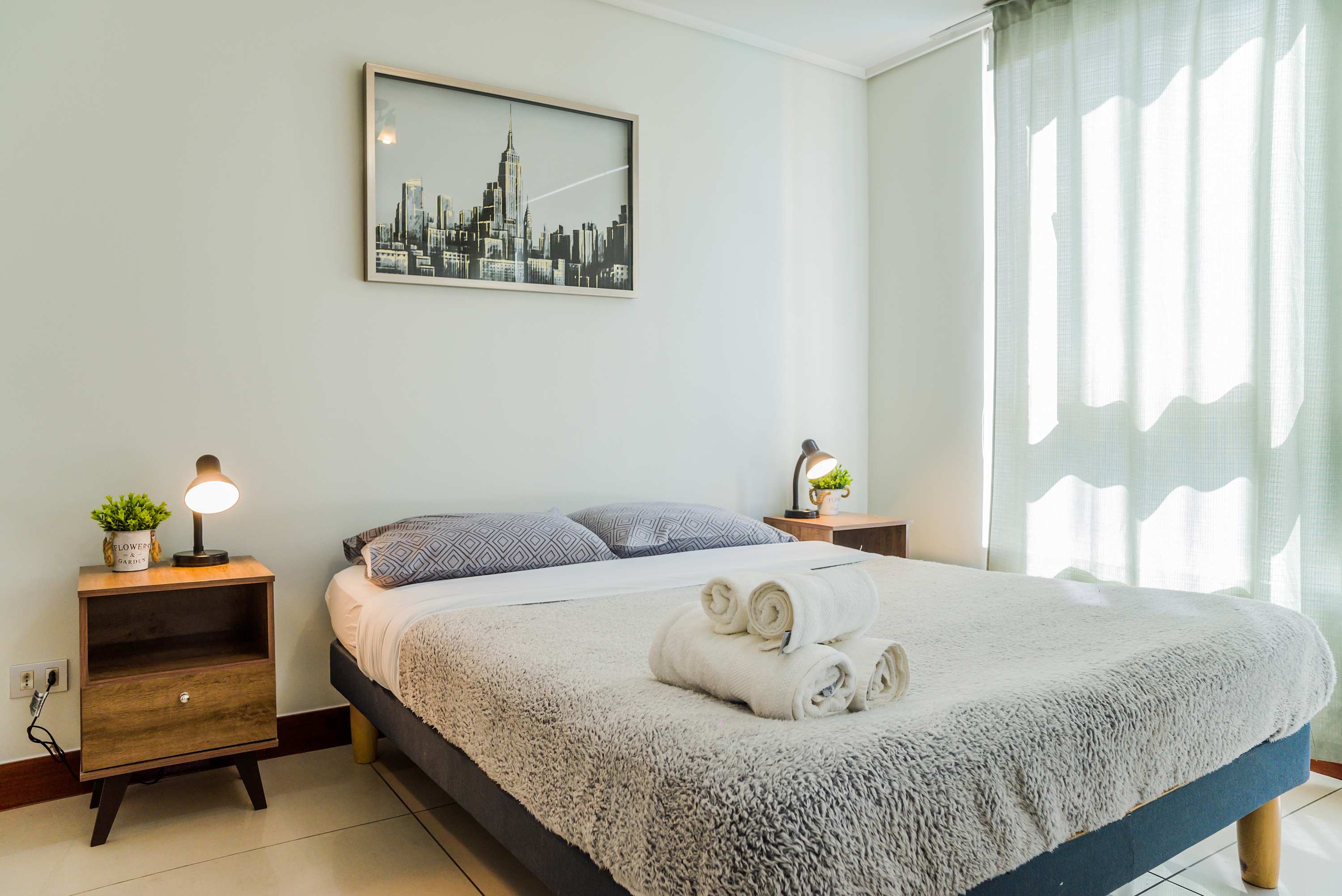 Private sleeping area with a textured bed, rolled towels, and bright natural light through sheer window shades.