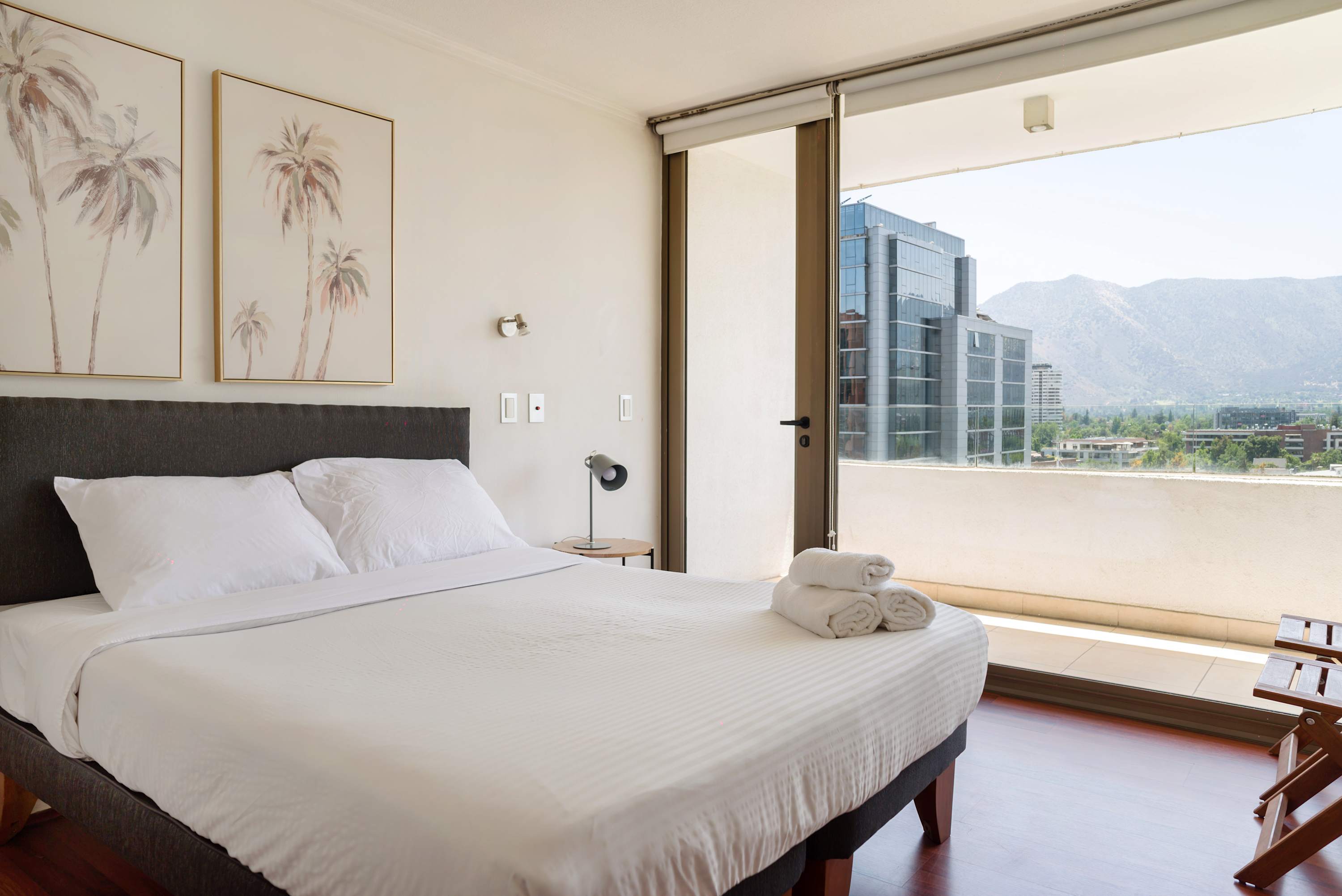 Bright bedroom with a king-size bed, rolled towels, and floor-to-ceiling glass doors opening to mountain views.