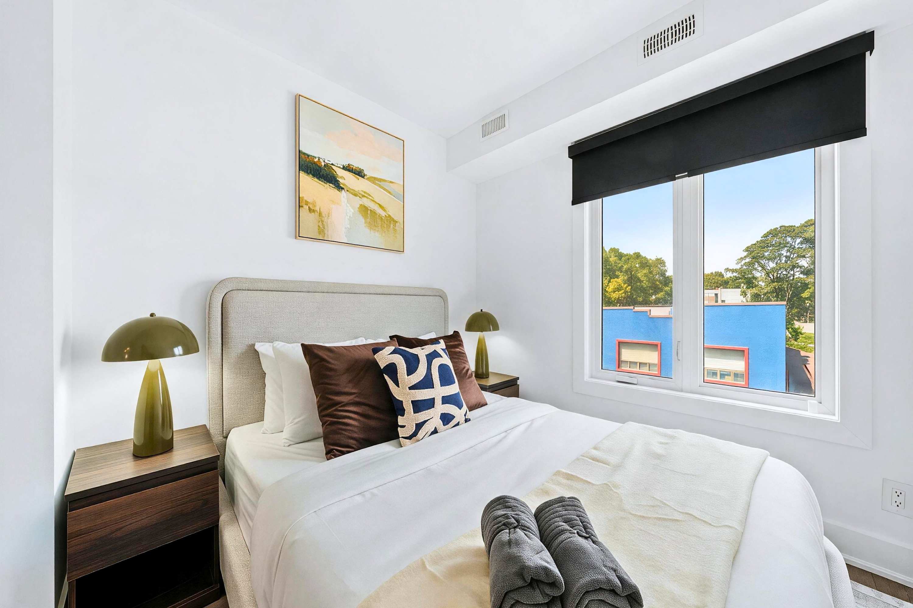 Quiet secondary queen bedroom with cozy bedside lamps and leafy street views.