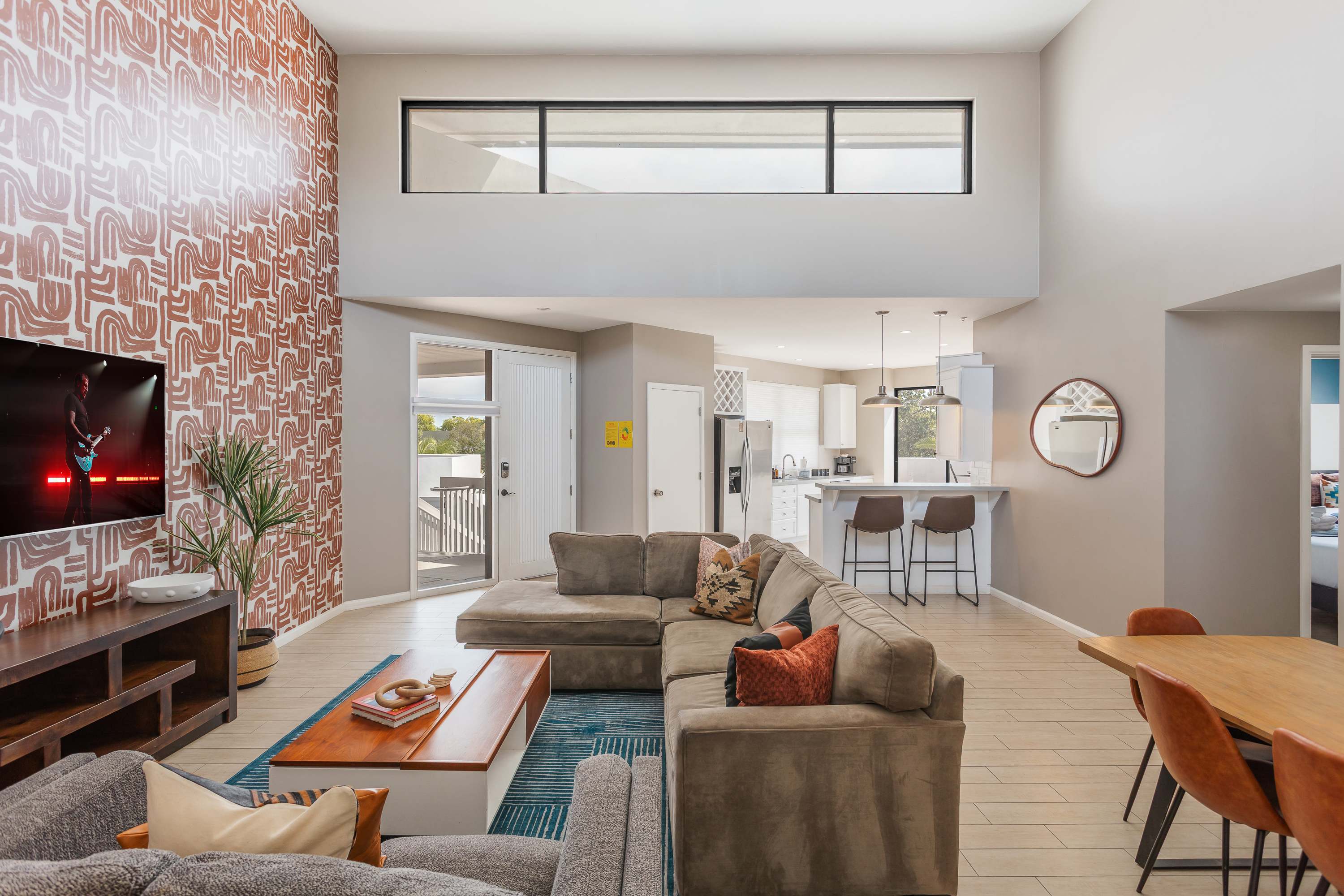 Spacious living room with soaring ceilings, a plush sectional, Smart TV, connection to dining area, and an open concept flow to the kitchen and easy access to the private balcony.