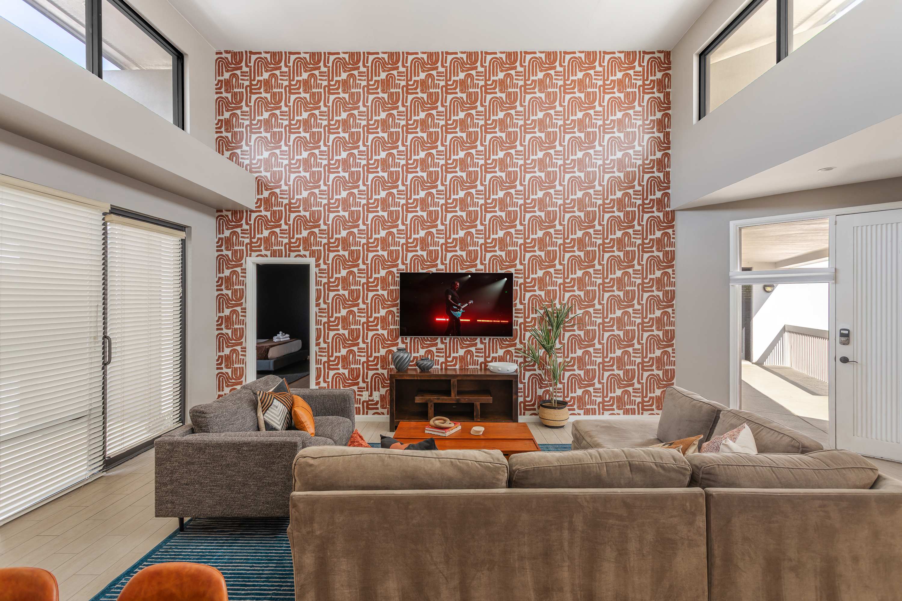 Spacious living room with soaring ceilings, a plush sectional, Smart TV, connection to dining area, and an open concept flow to the kitchen and easy access to the private balcony.