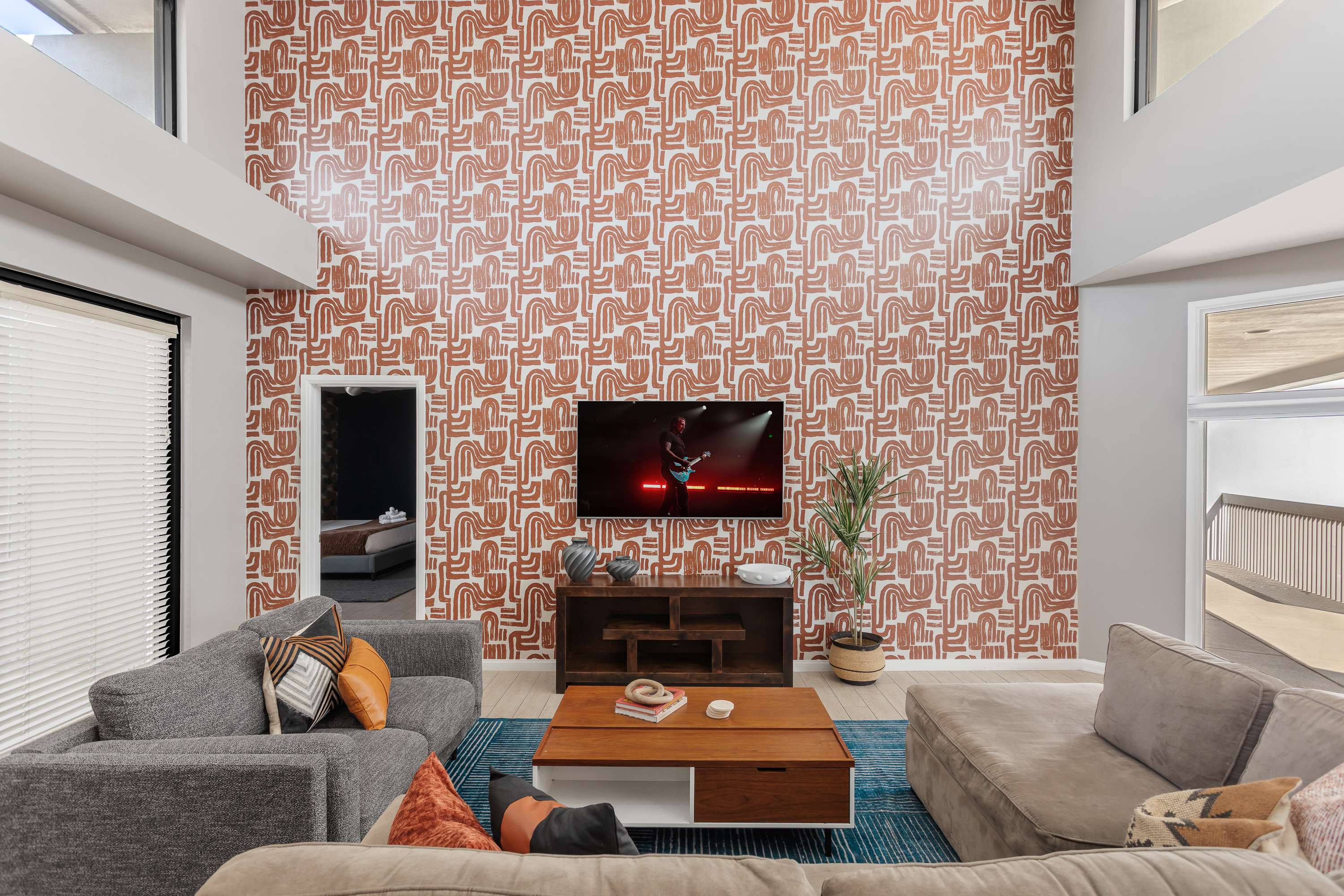 Spacious living room with soaring ceilings, a plush sectional, Smart TV, connection to dining area, and an open concept flow to the kitchen and easy access to the private balcony.