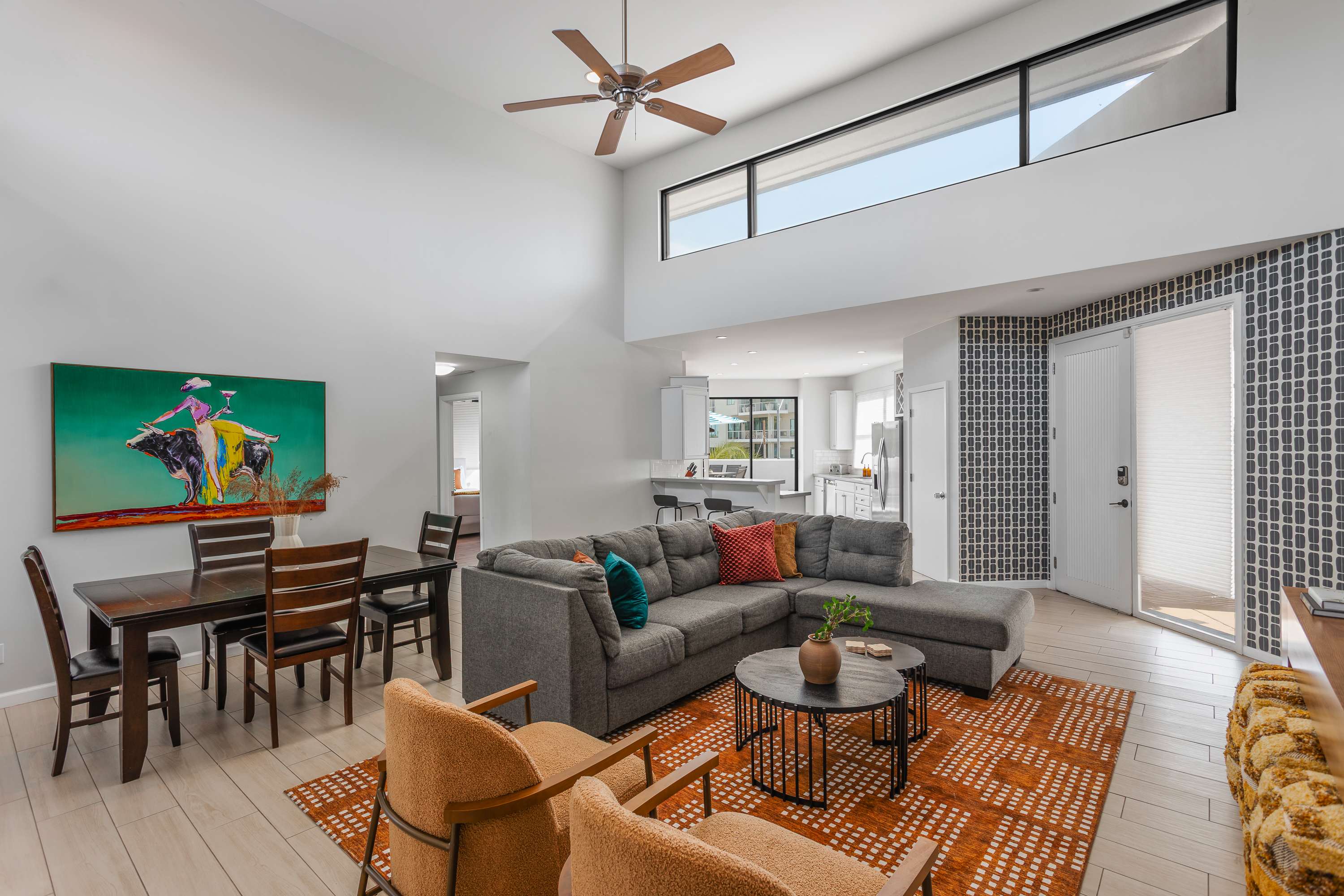 Bright and open living room with soaring ceilings, oversized windows, a plush sectional, Smart TV, and easy flow to the dining area for 4, kitchen, and balcony.