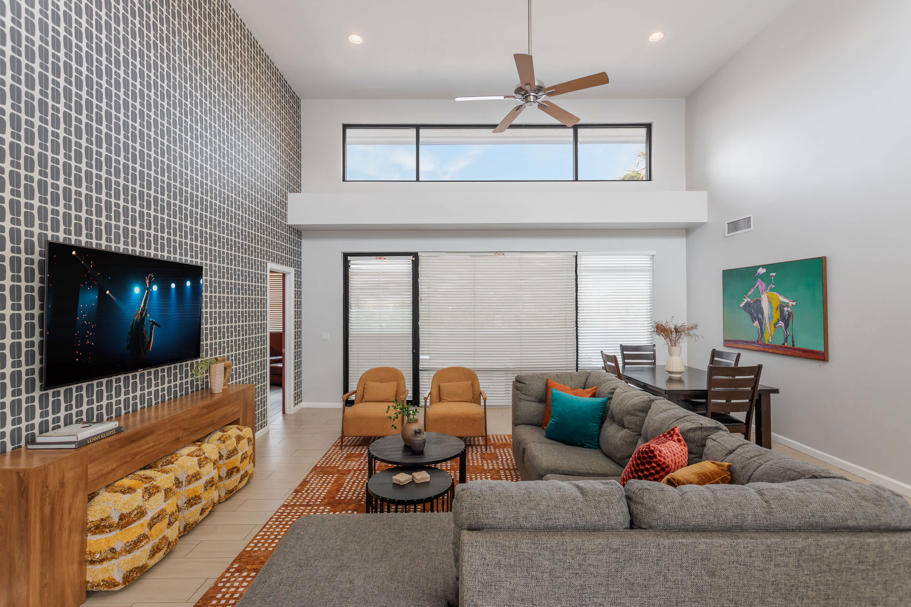 Bright and open living room with soaring ceilings, oversized windows, a plush sectional, Smart TV, and easy flow to the dining area for 4, kitchen, and balcony.