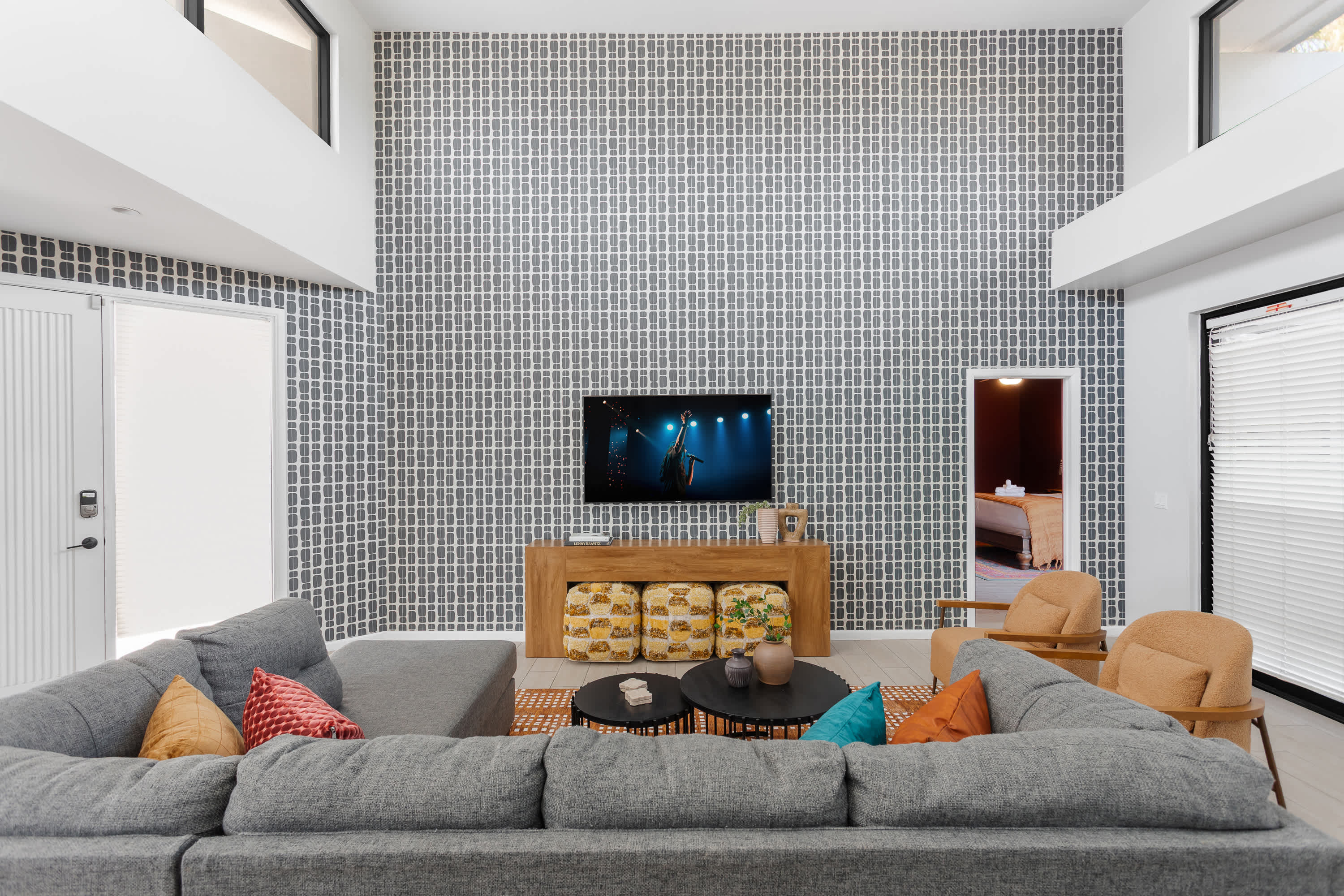 Bright and open living room with soaring ceilings, oversized windows, a plush sectional, Smart TV, and easy flow to the dining area for 4, kitchen, and balcony.