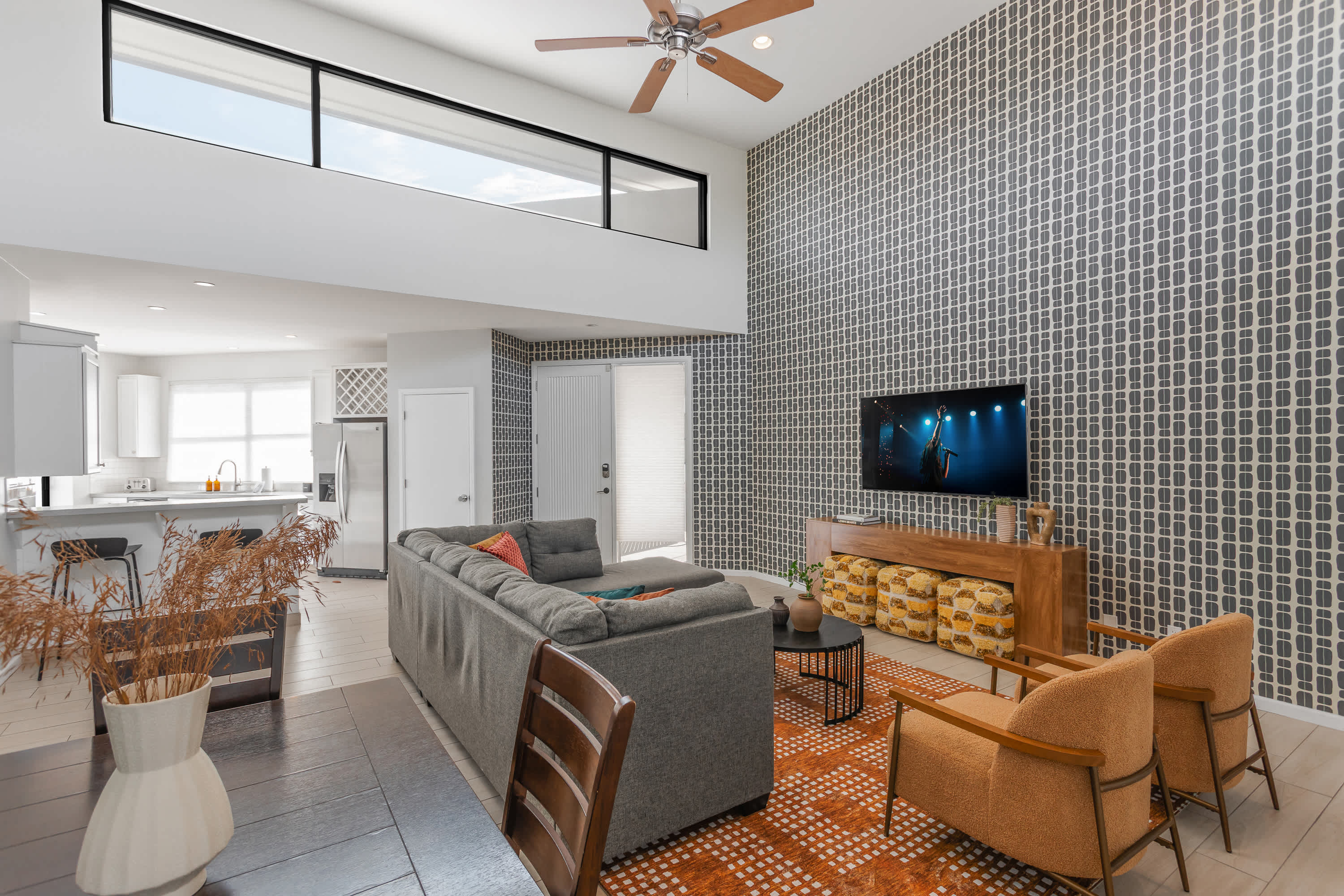 Bright and open living room with soaring ceilings, oversized windows, a plush sectional, Smart TV, and easy flow to the dining area for 4, kitchen, and balcony.