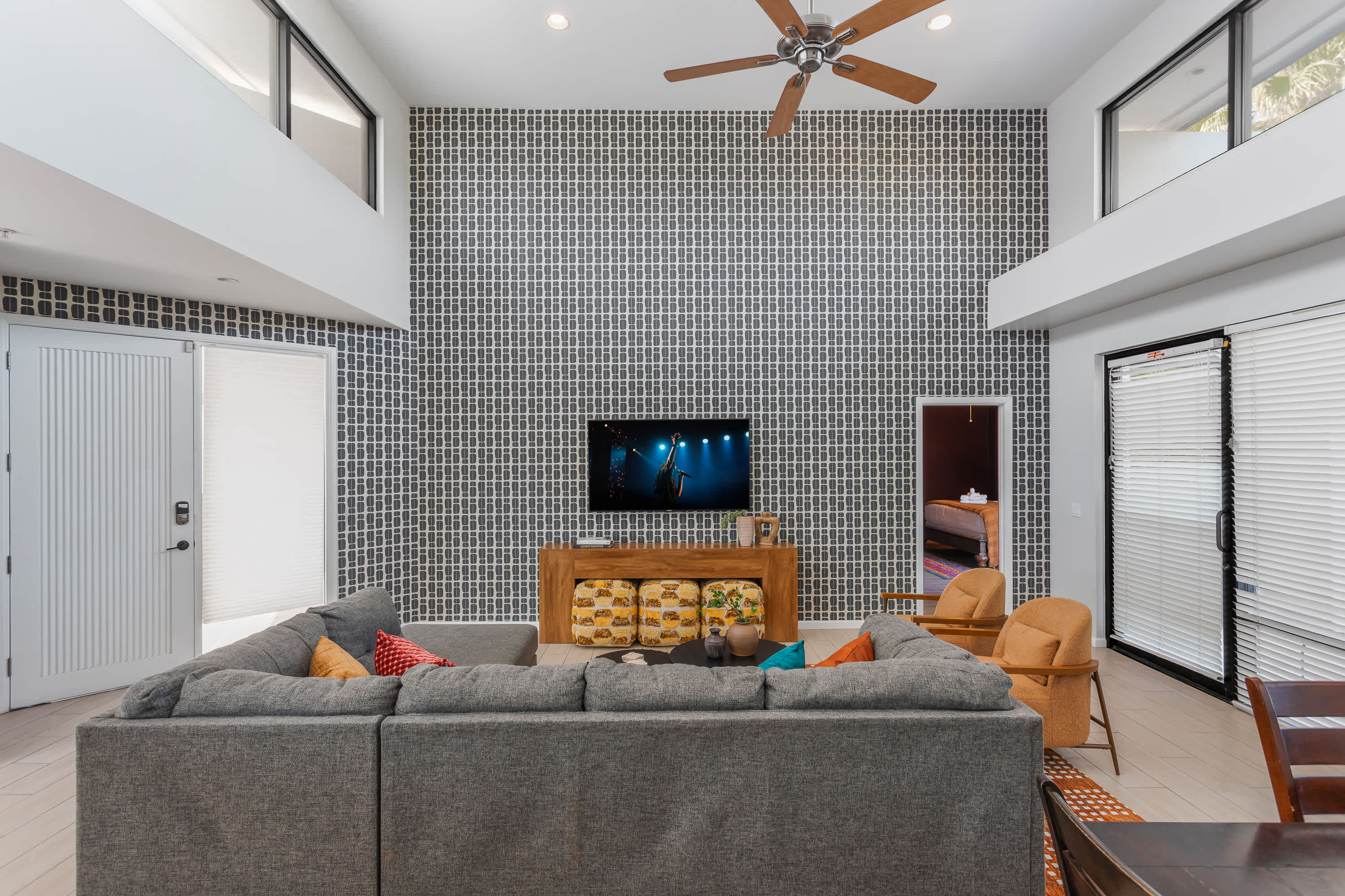 Bright and open living room with soaring ceilings, oversized windows, a plush sectional, Smart TV, and easy flow to the dining area for 4, kitchen, and balcony.