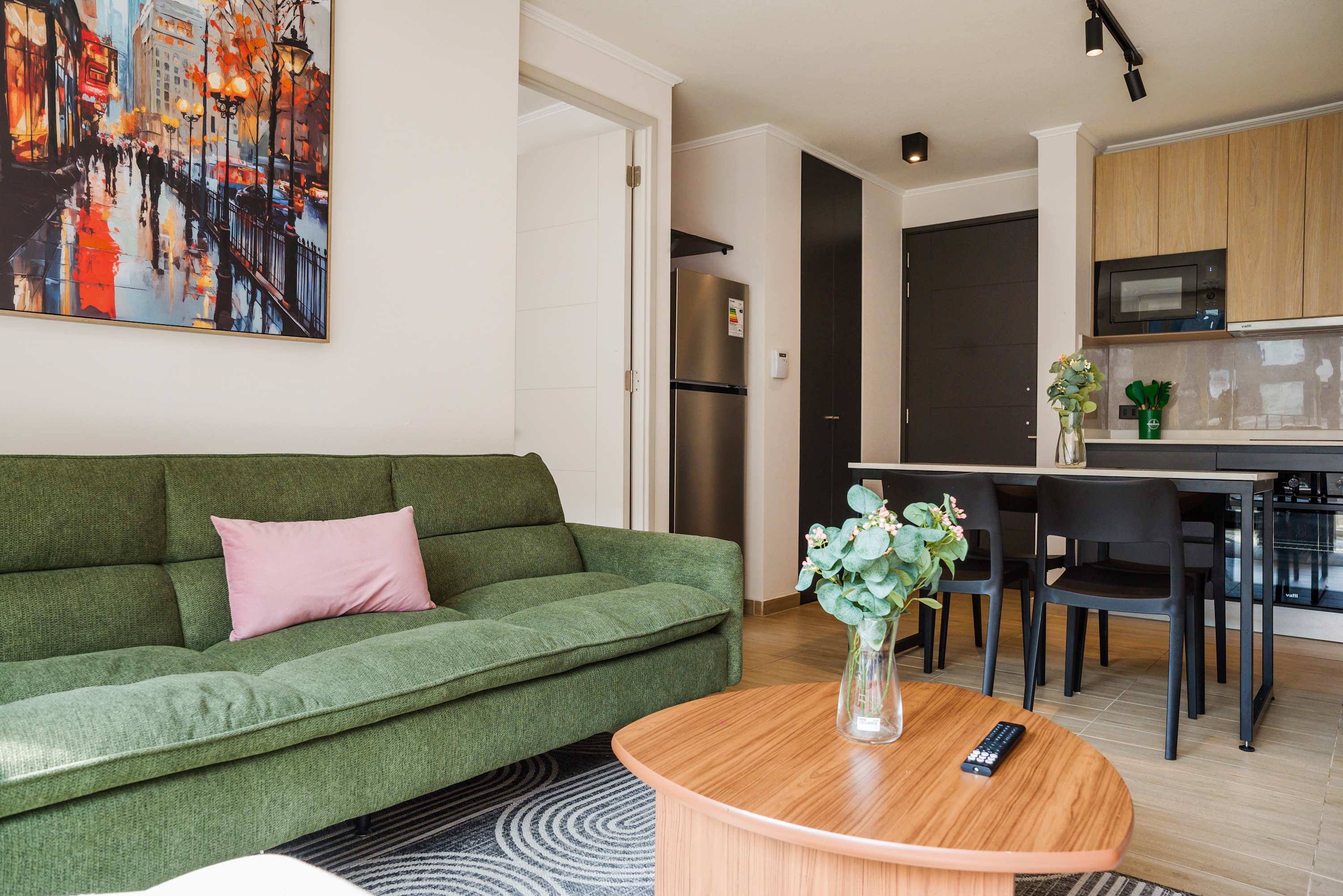 Comfortable living room with a green sectional, colorful cityscape artwork, and an open kitchen-dining area for relaxed stays.