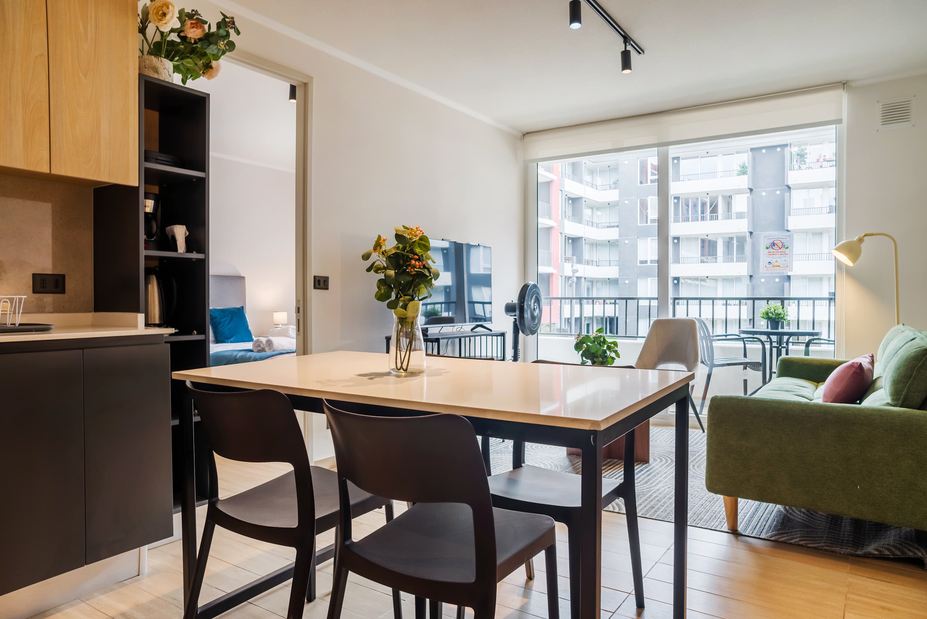 Open-plan dining area with seating for four, a contemporary kitchen, and expansive windows overlooking the apartment courtyard.