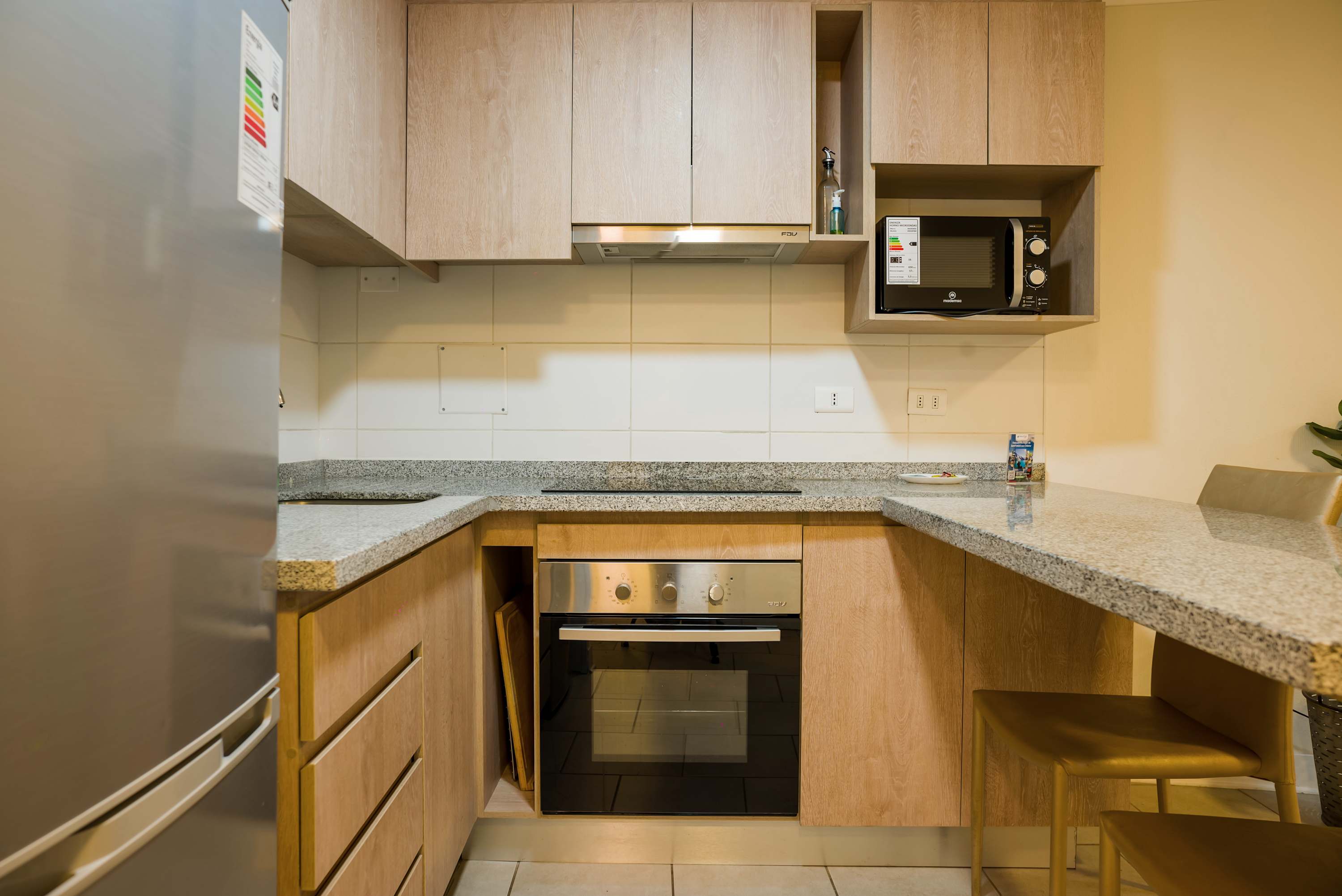 Private kitchen with light oak cabinetry, granite counters, built-in oven, microwave, and a compact dining counter for two.