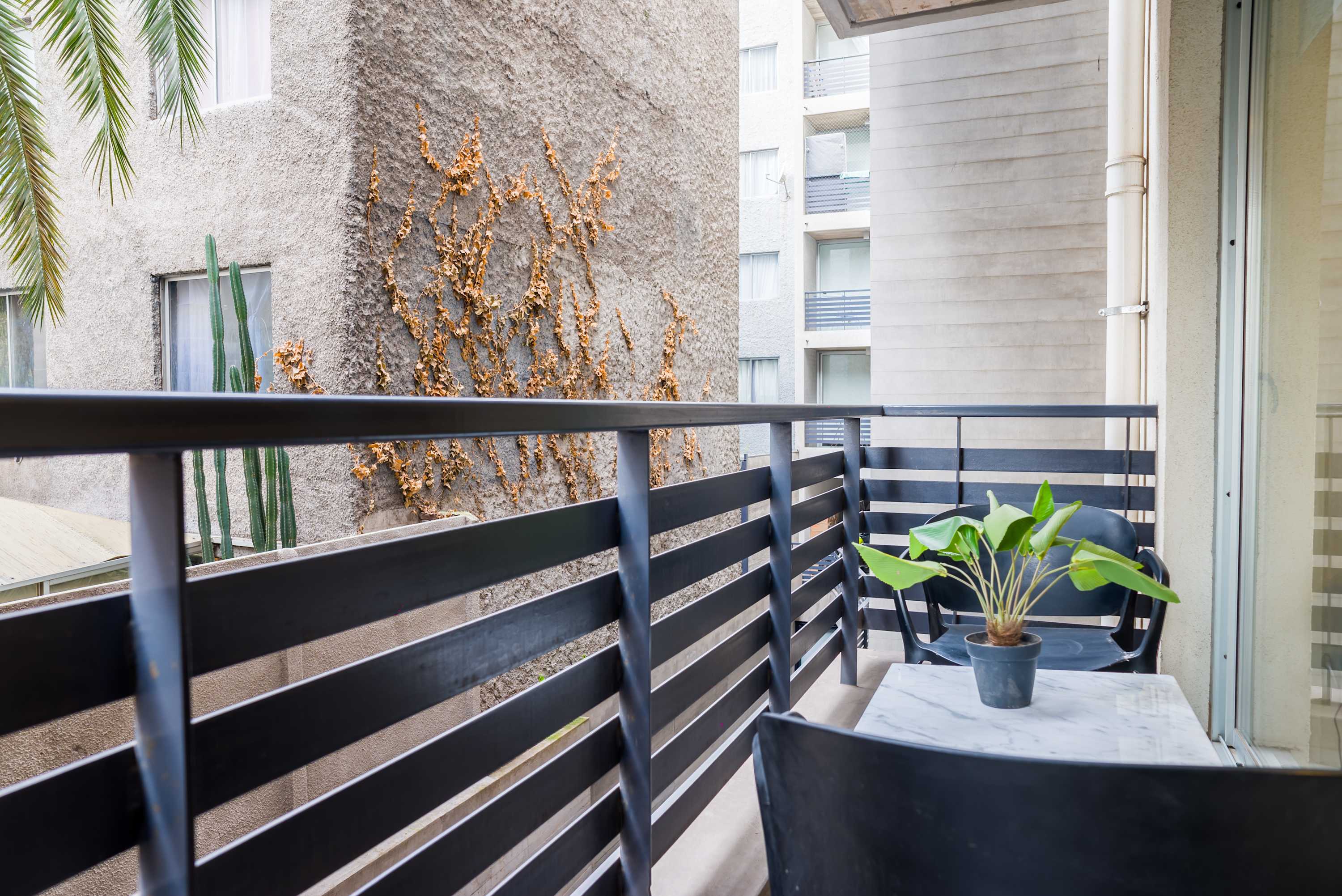 Private balcony with two chairs, a marble-look table, and leafy greenery for enjoying fresh air outdoors.