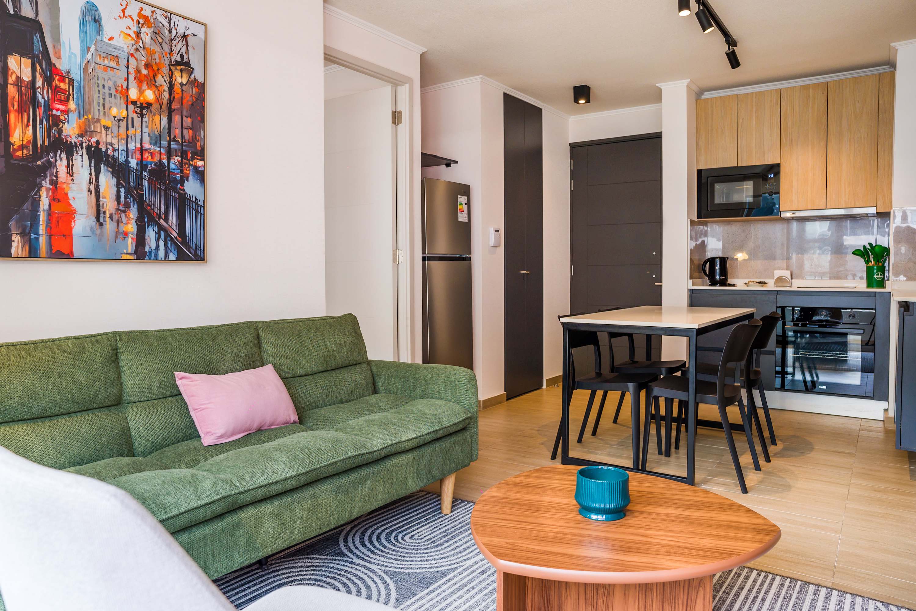 Private living room with a green sectional, colorful cityscape artwork, and a fully equipped open kitchen with breakfast seating.