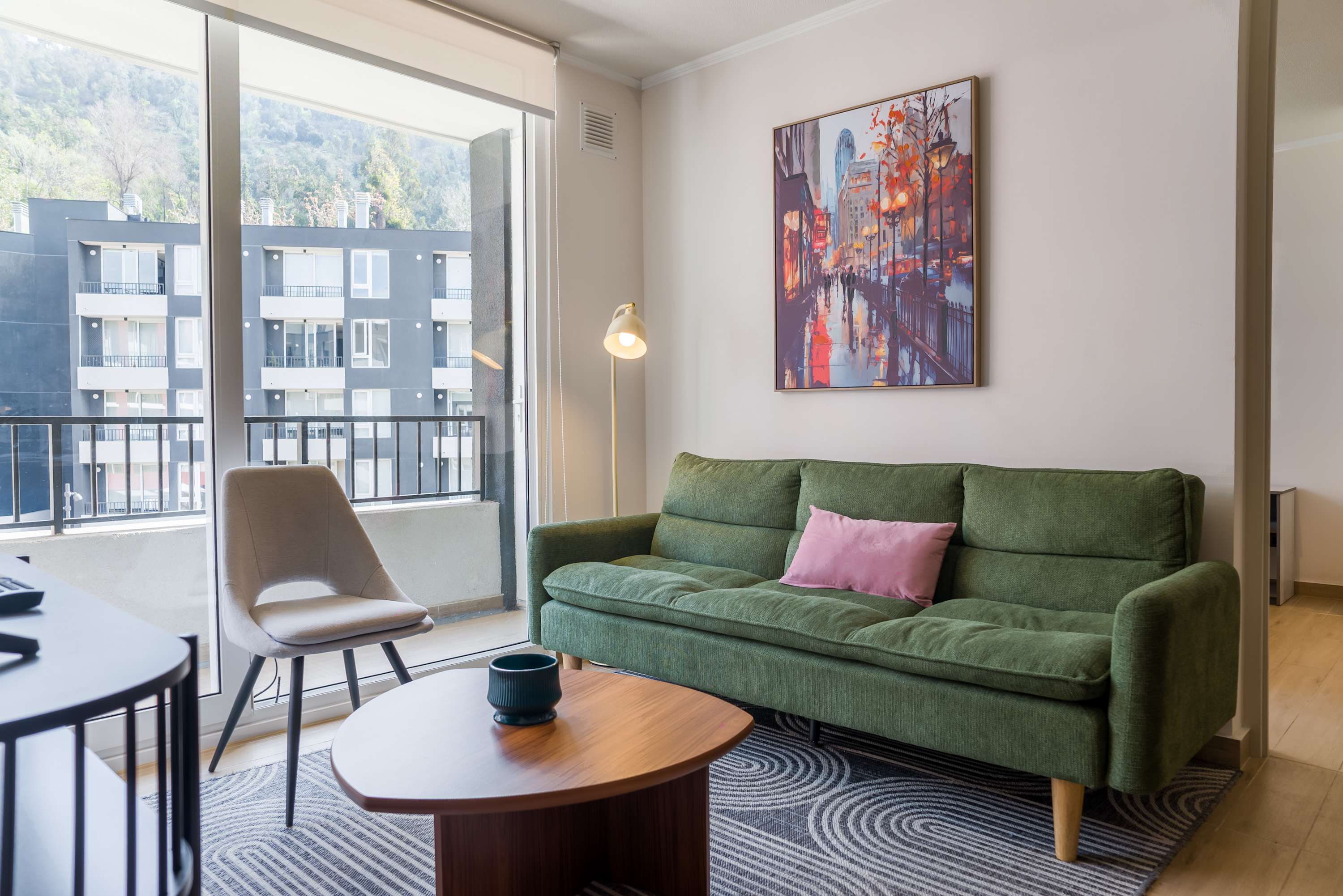Private living room with a green sofa, colorful artwork, and a large window overlooking a wooded hillside.