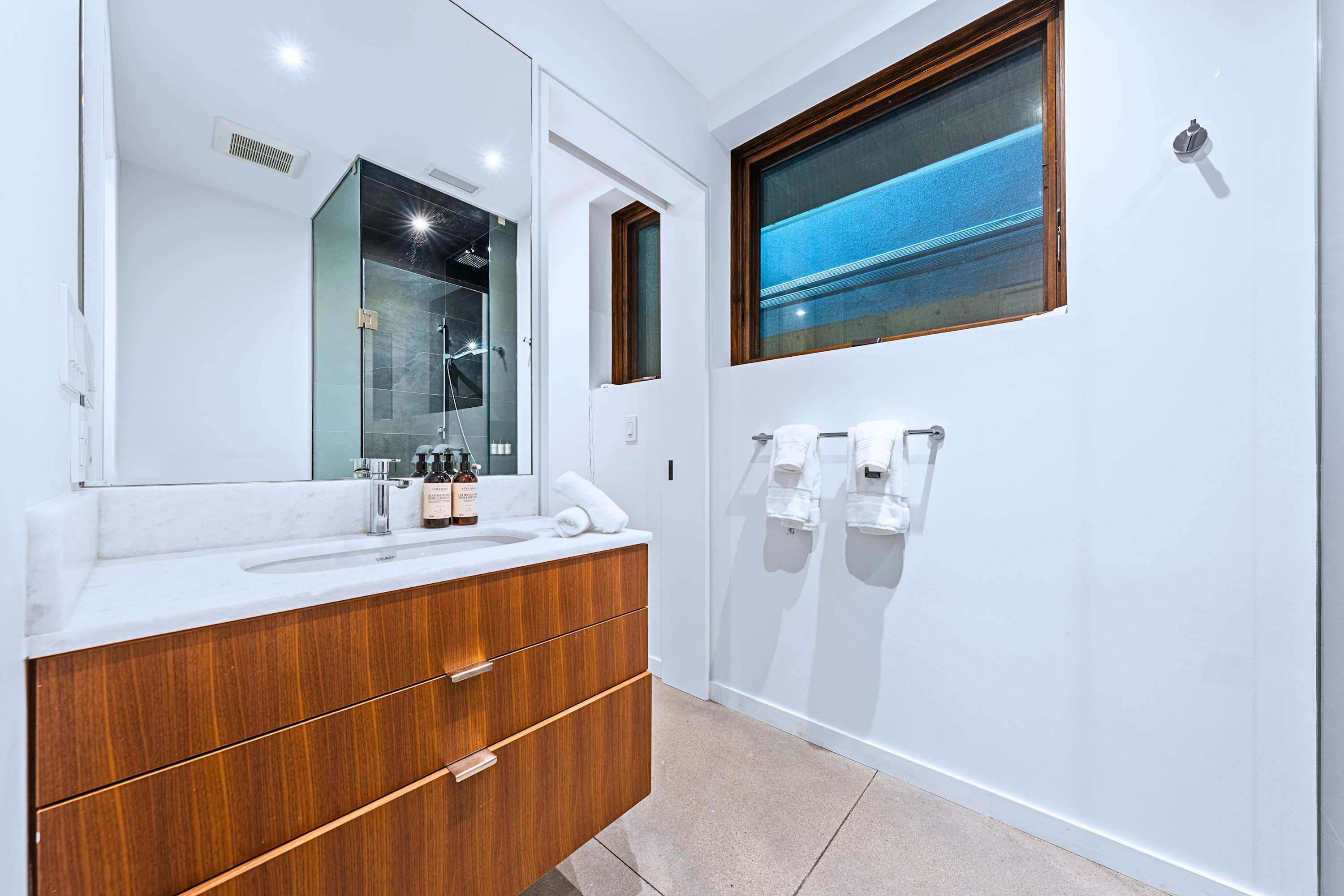 Floating vanity with oversized mirror, hotel-grade towels, and bright, clean illumination.
