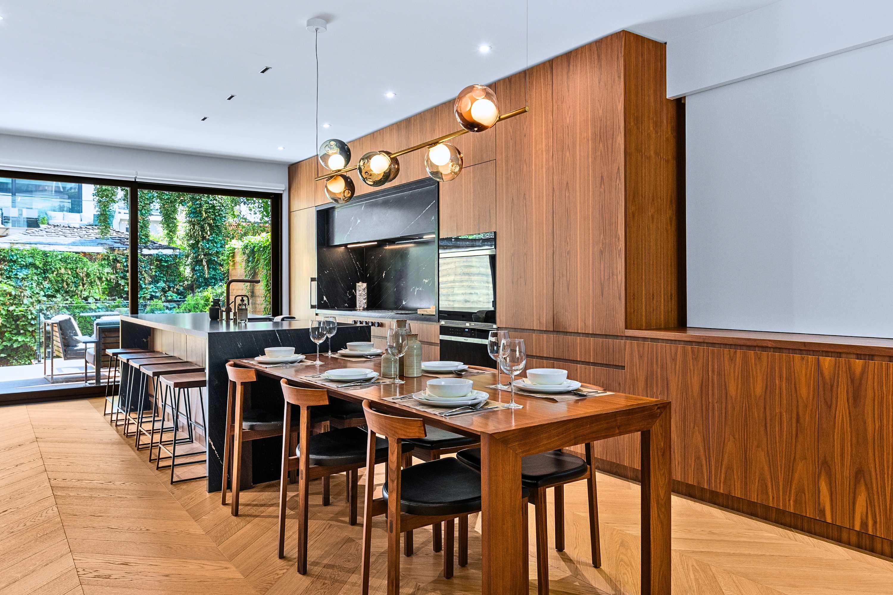 Long dining table anchored by custom wood paneling and warm ambient lighting.