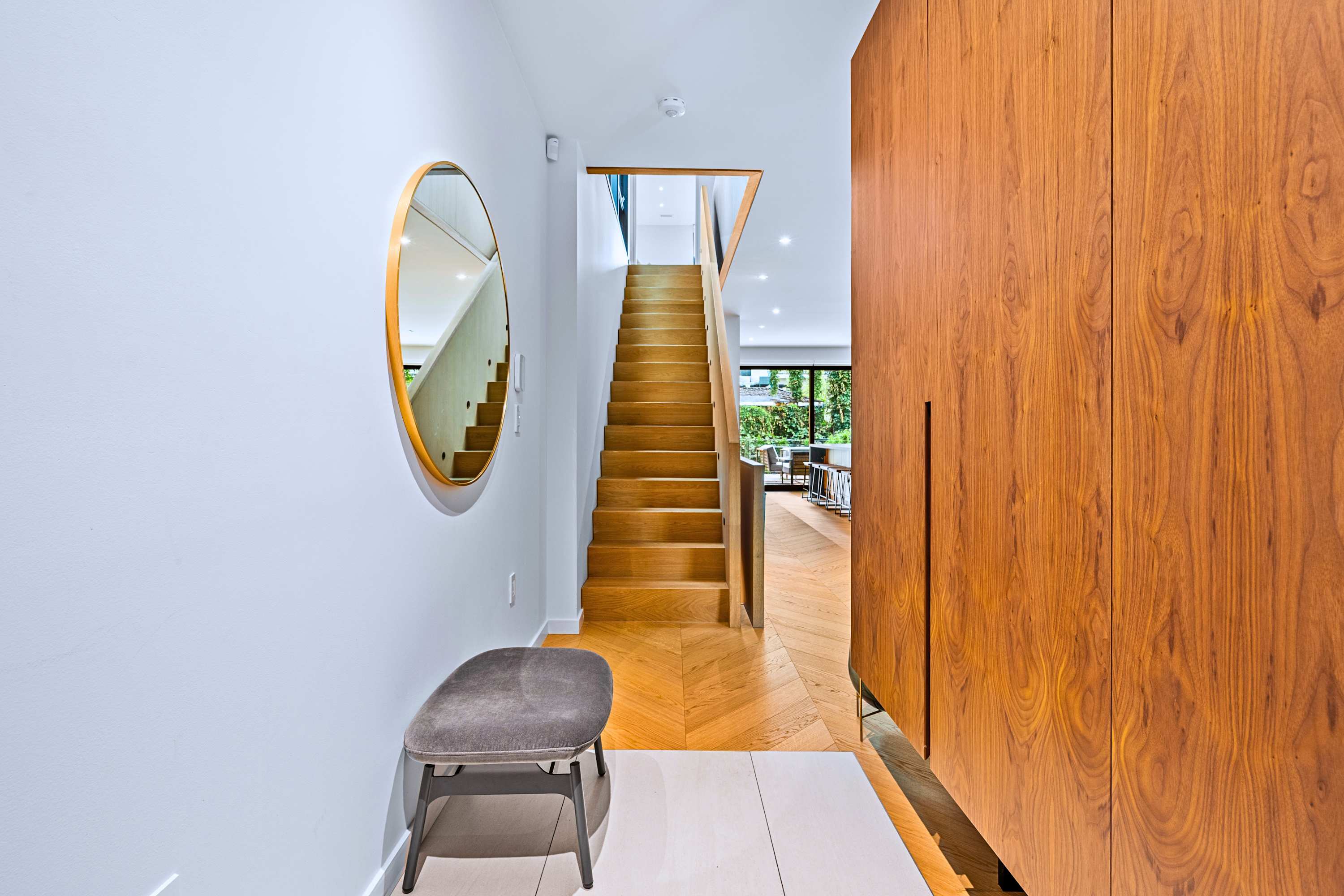 Seamless hallway entry with warm wood built-ins and floating staircase.