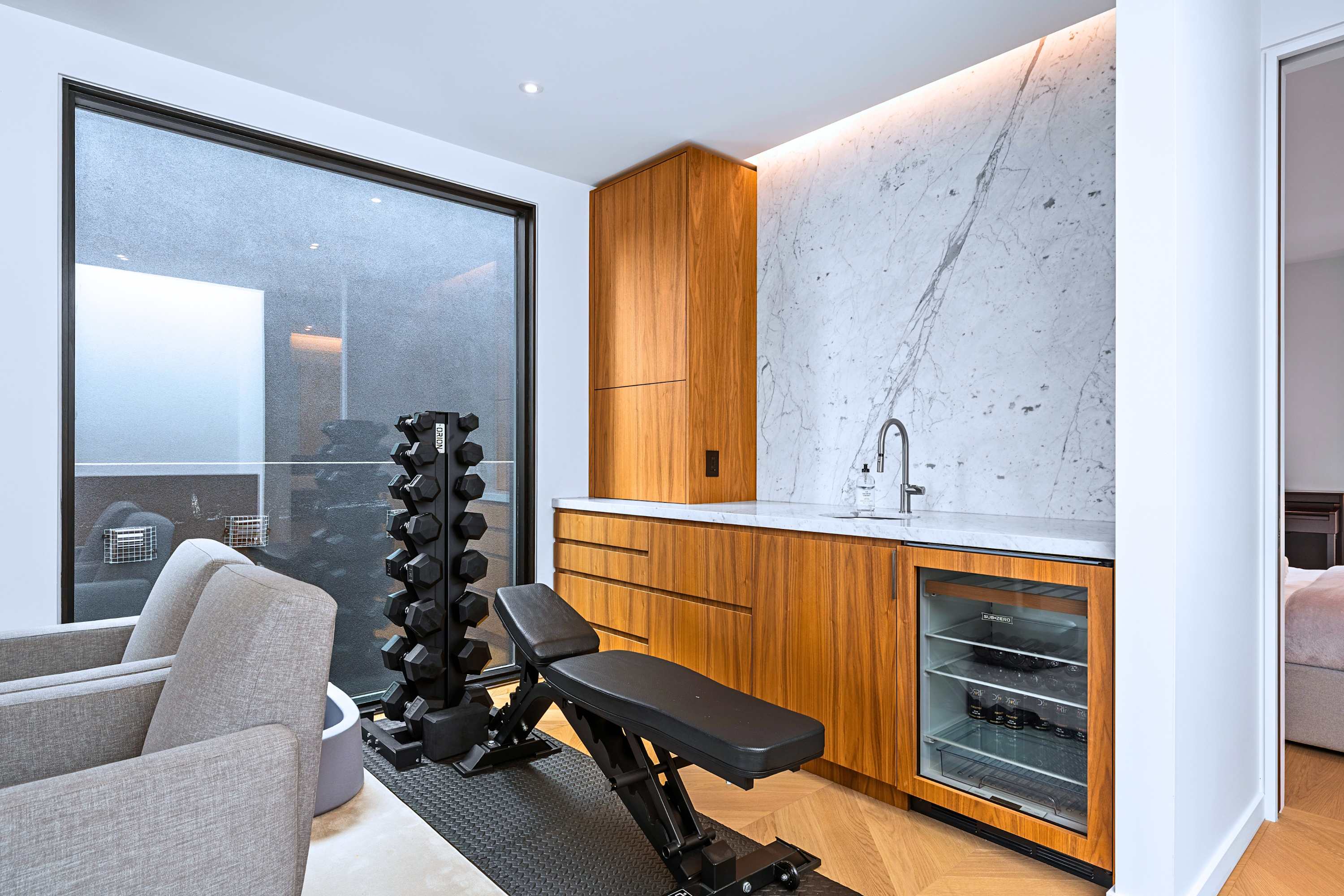 In-home fitness corner with weight rack, exercise bench, and mini beverage fridge.